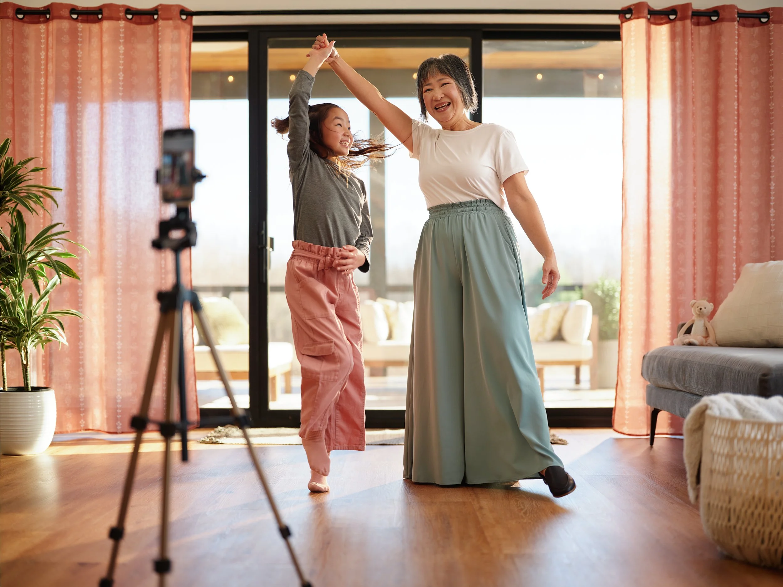 Family dancing in a living room while filming on a phone mounted on a tripod, representing health and wellbeing lifestyle.