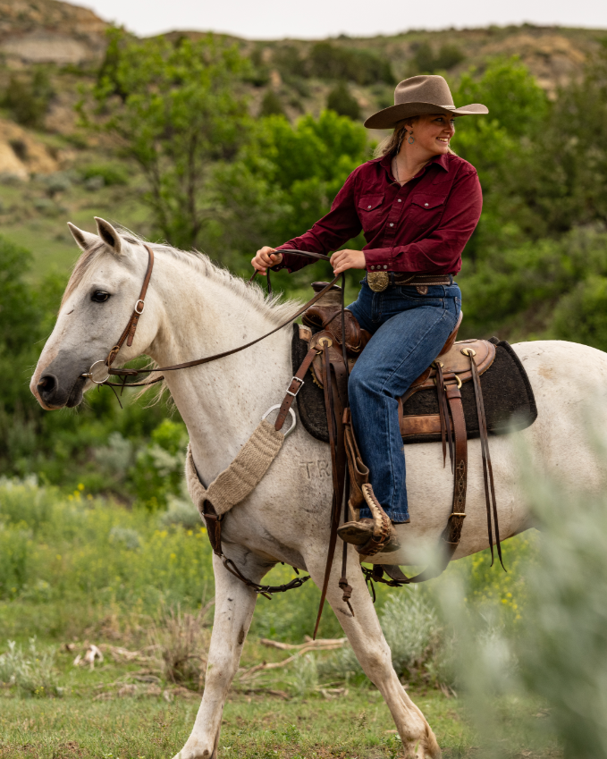 Equestrian rider smiling while riding a horse and looking behind her.