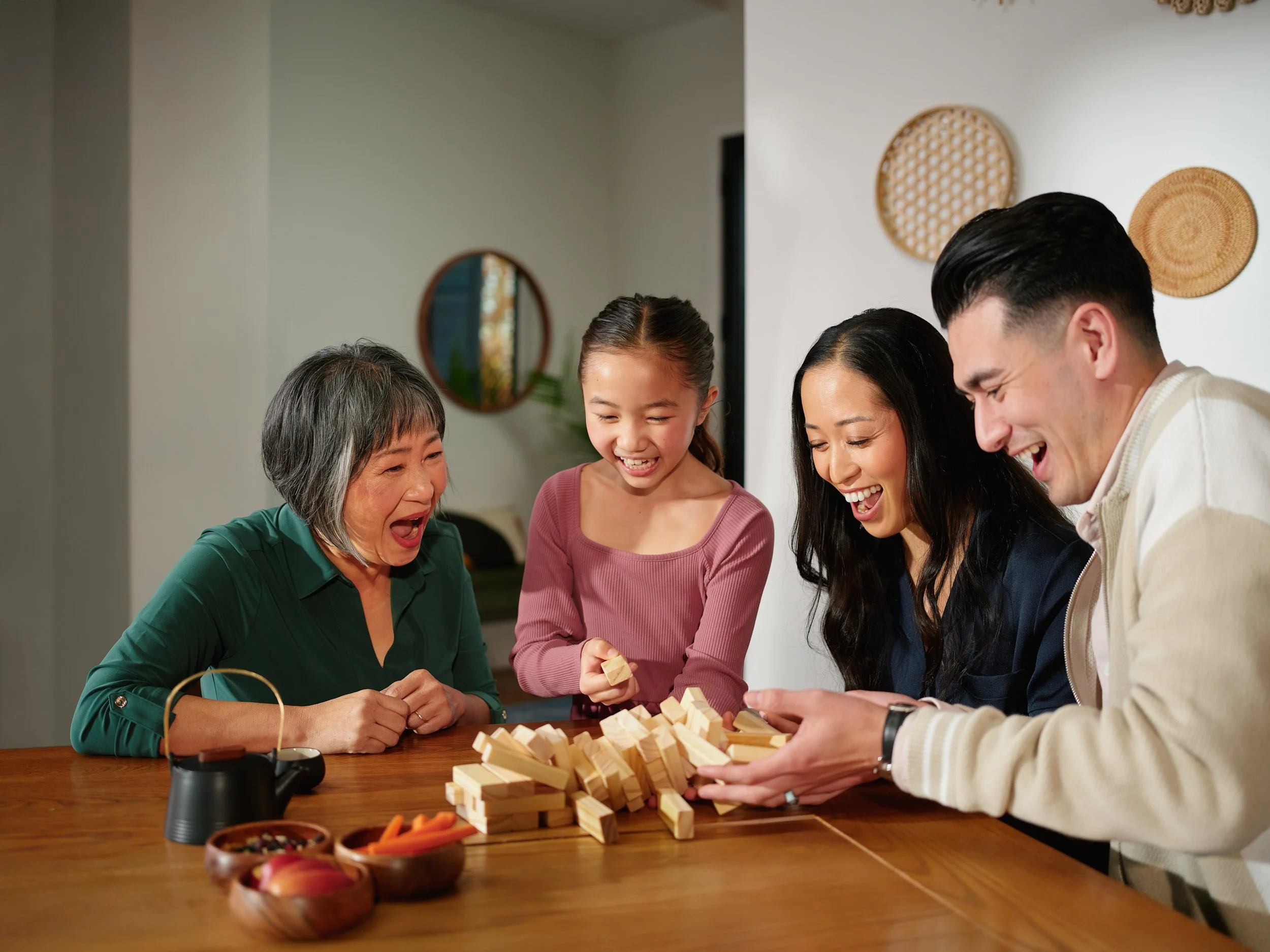 Family laughing while playing Jenga, representing a joyful health and wellbeing moment.