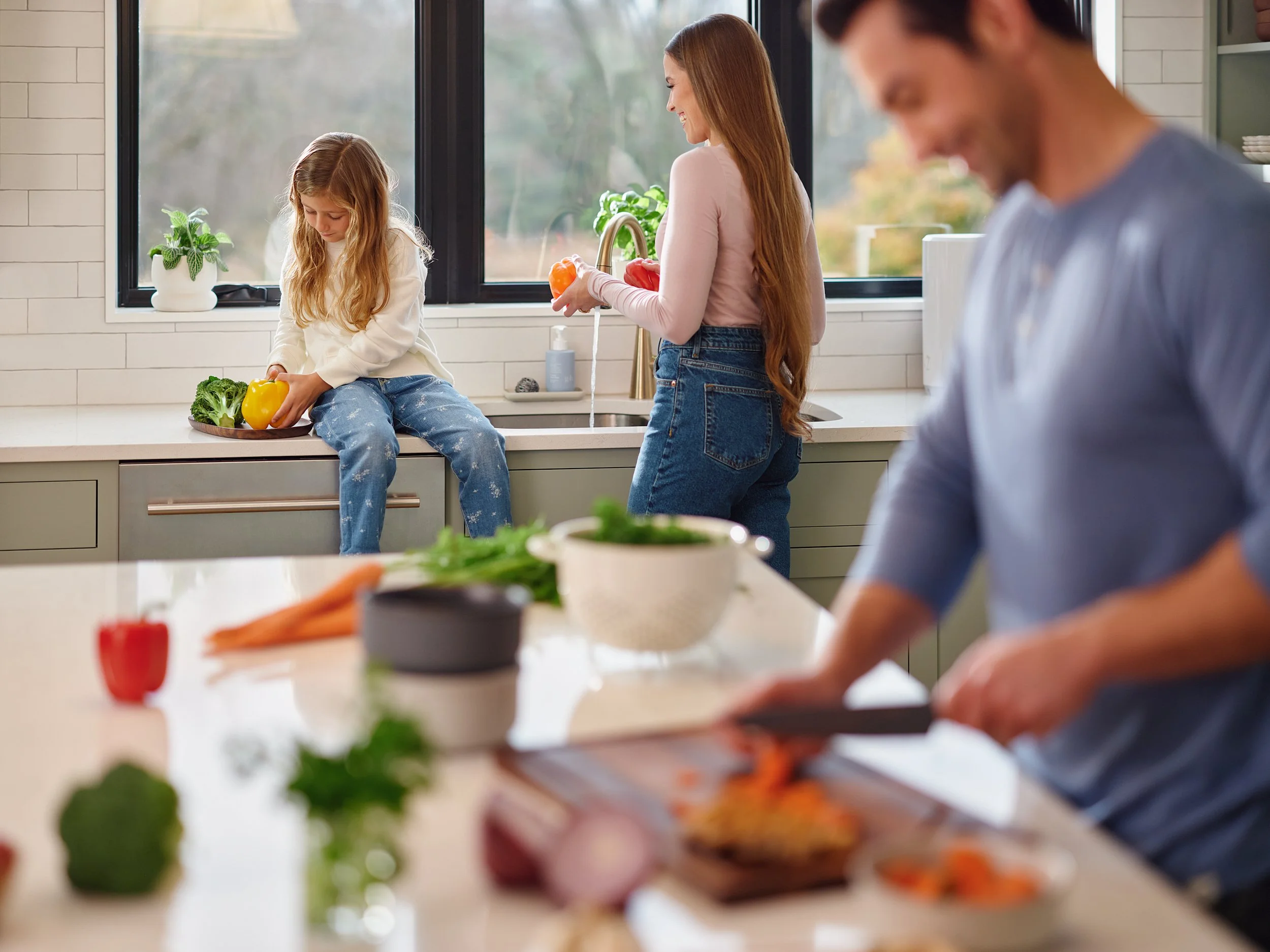Parents and daughter in a kitchen with the father chopping vegetables, representing a health and wellbeing lifestyle.