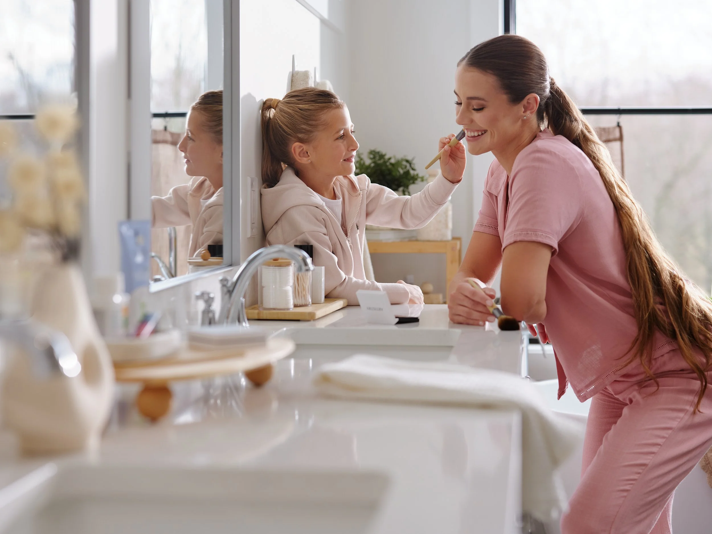 Daughter applying makeup to her mother as both smile happily, representing a joyful health and wellbeing moment.