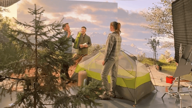 Behind the scenes on a video shoot with crew on set and a tent prop in a staged environment.