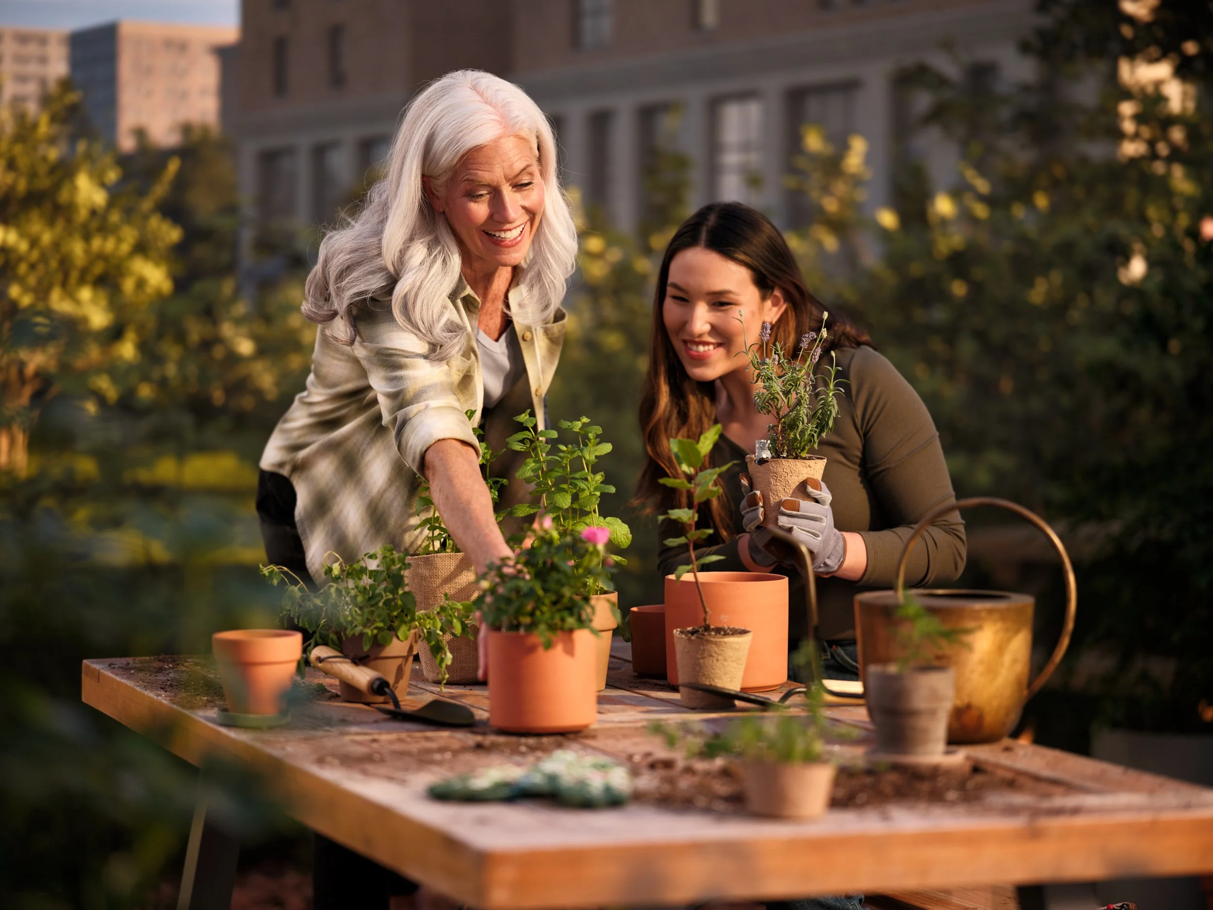 Two women potting plants on a table outdoors.