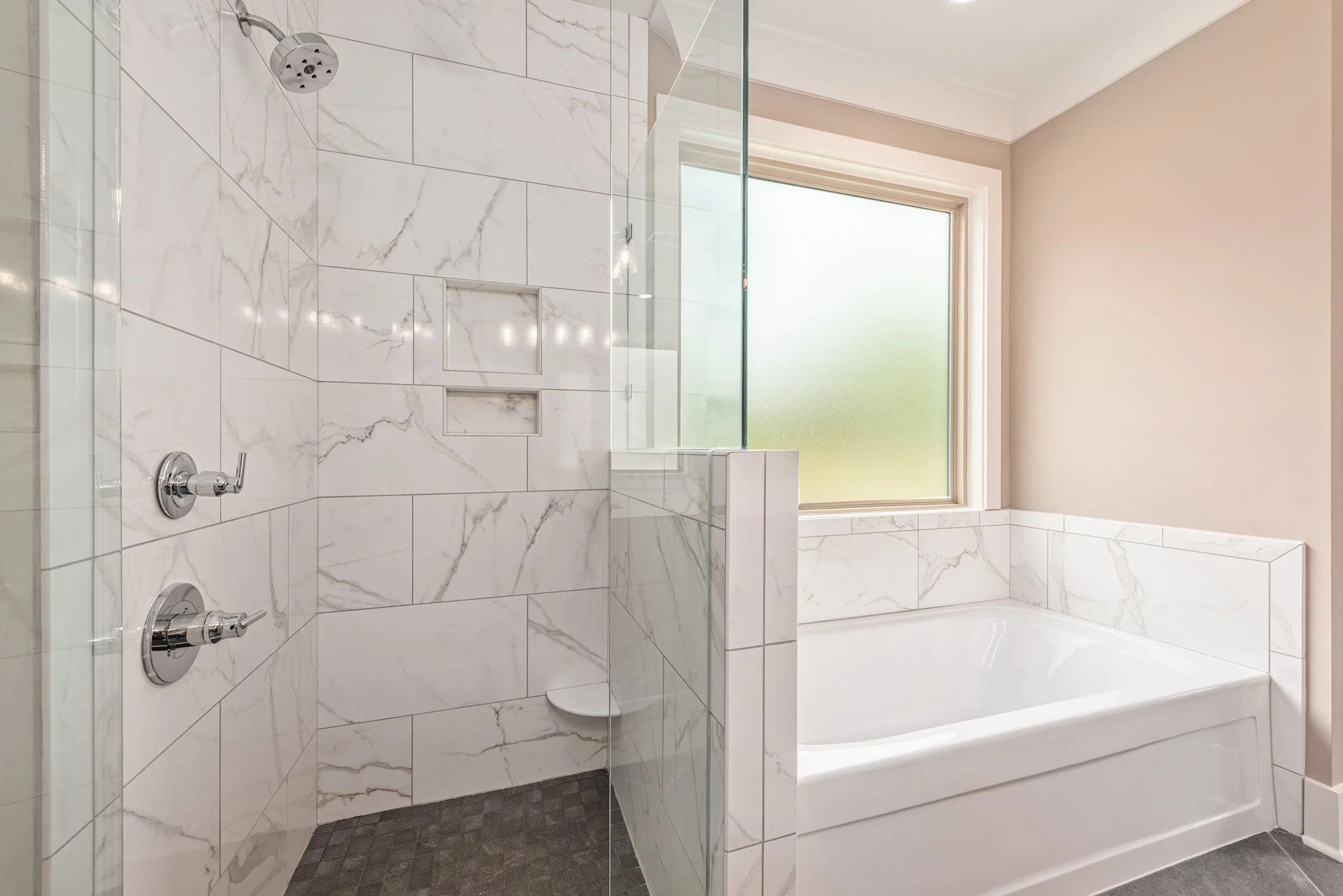 Modern bathroom with a marble-tiled shower and tub, featuring a glass shower door and frosted window.