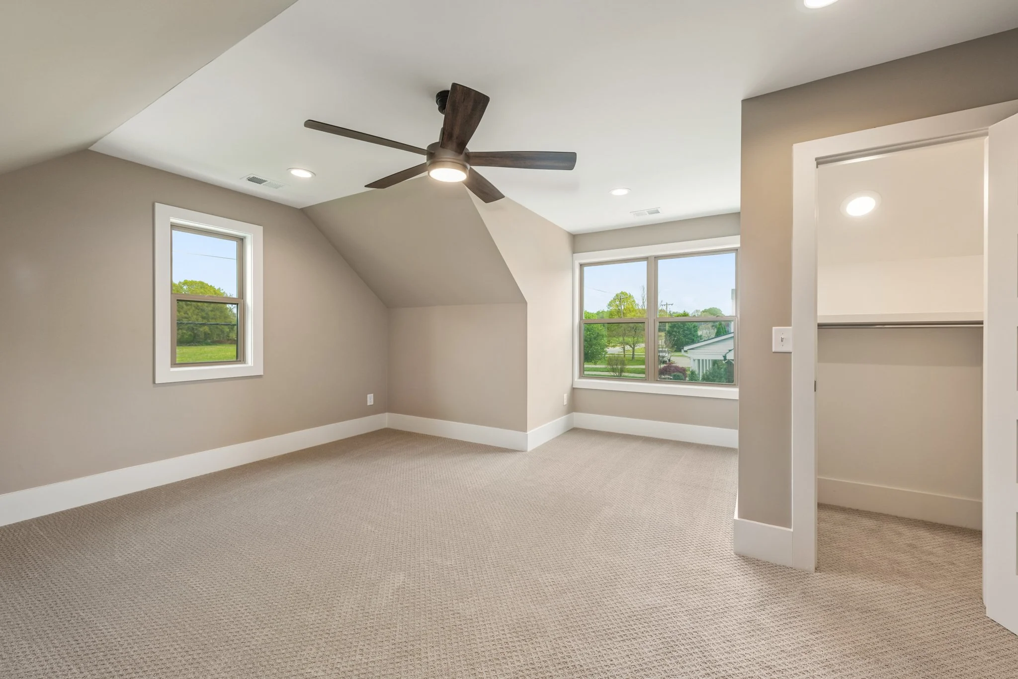Empty carpeted room with a ceiling fan, recessed lighting, two windows, and an open closet door.