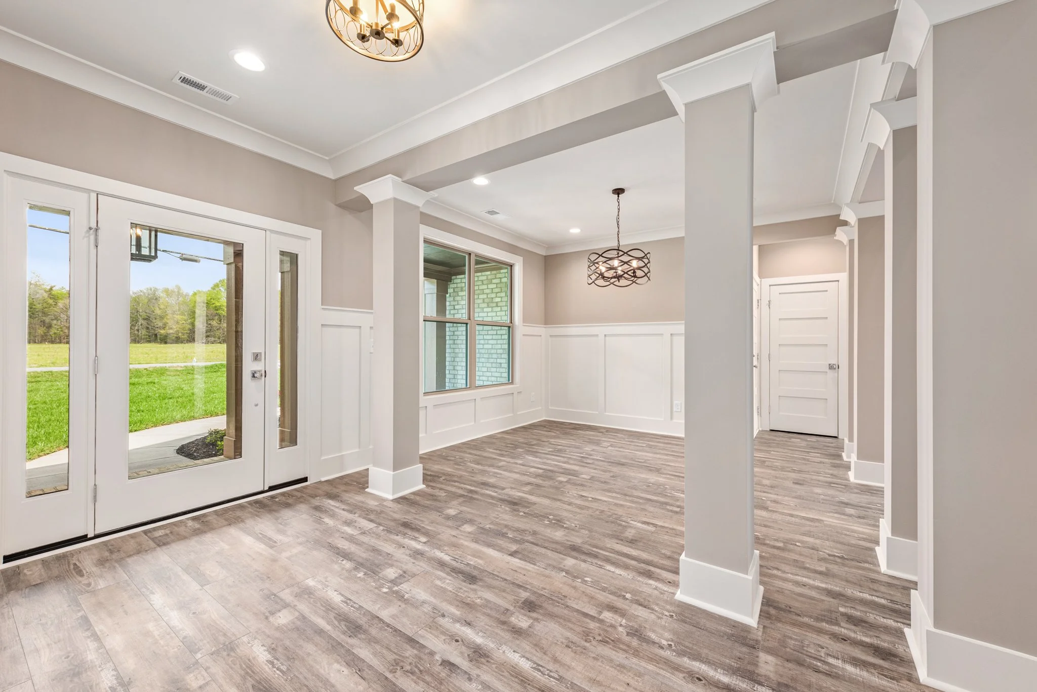 Empty room with hardwood flooring, large windows, and double glass doors facing a green lawn.