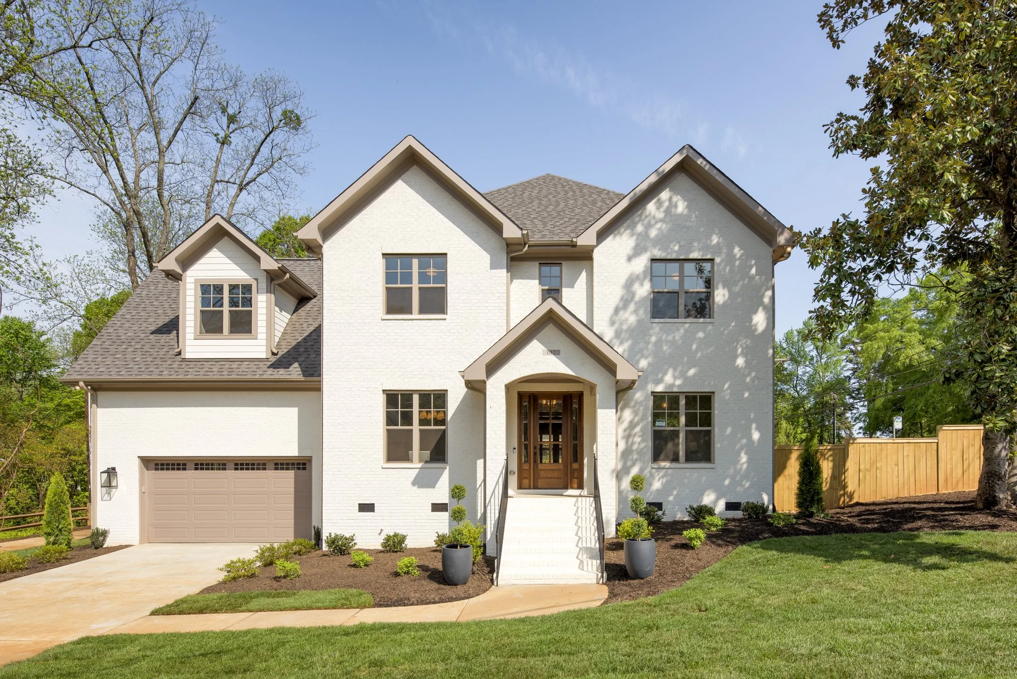 Modern two-story house with white brick exterior, brown garage door, and landscaped front yard with grass and potted plants.