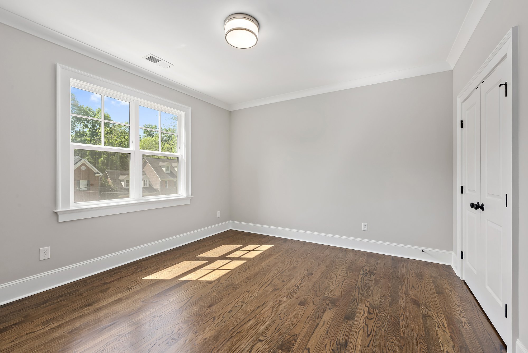Empty room with hardwood floor, gray walls, white trim, and a large window with natural light.