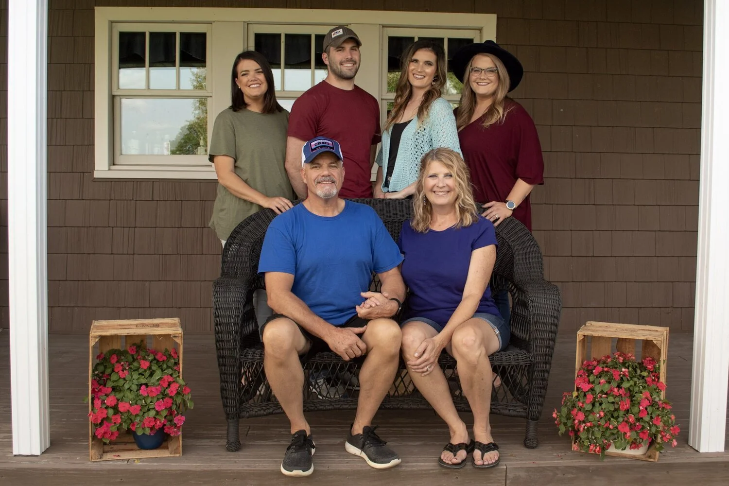 Melissa Doll poses with her husband and 4 children on a front porch with red flowers.