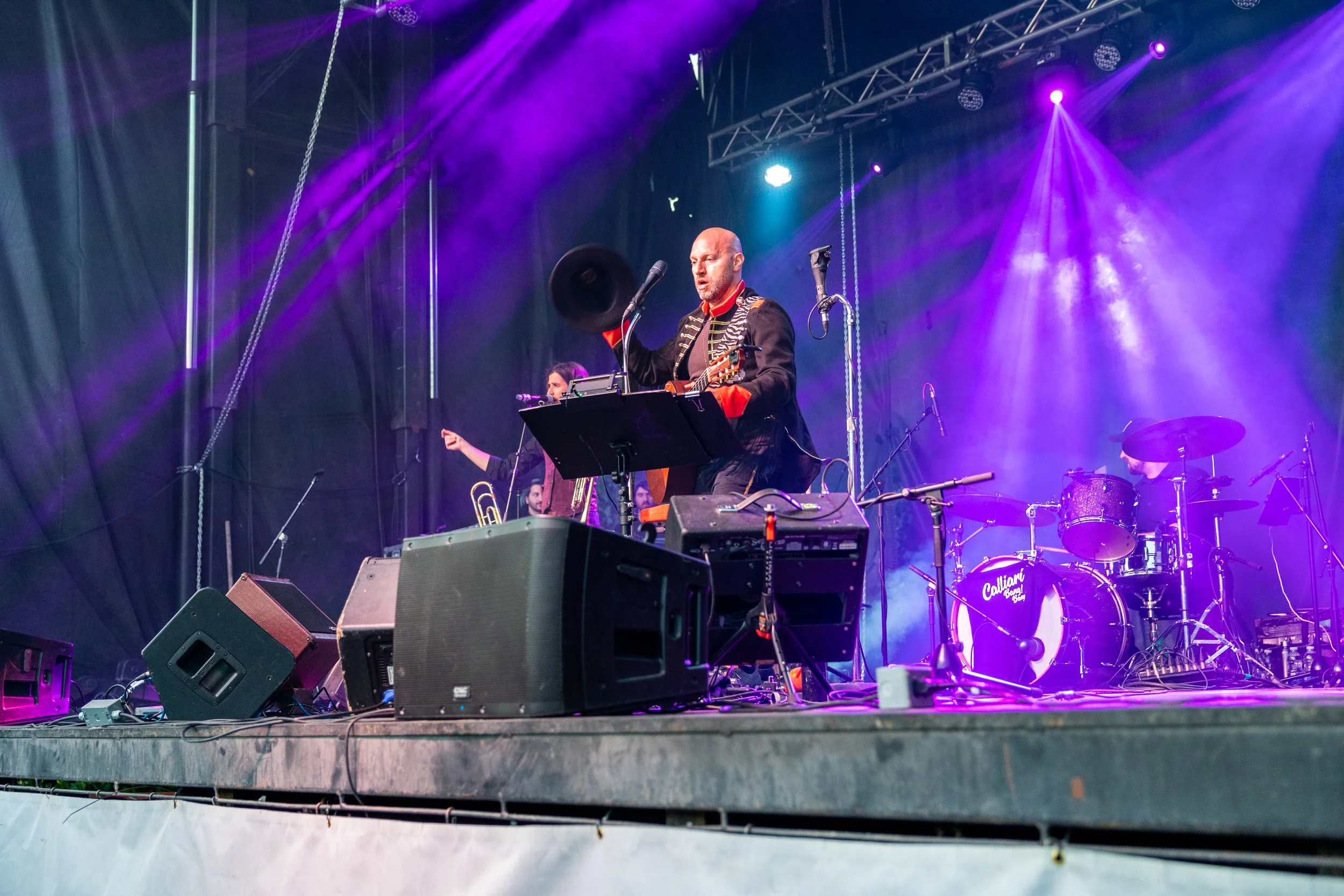 Musical performance on stage with a band, featuring a musician playing guitar and singing into a microphone under colorful stage lights.