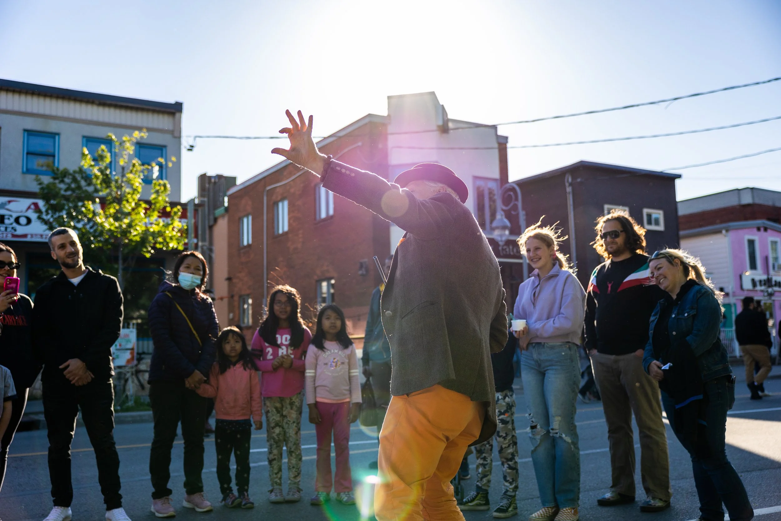 Street performer entertaining a crowd of adults and children in an urban area on a sunny day.