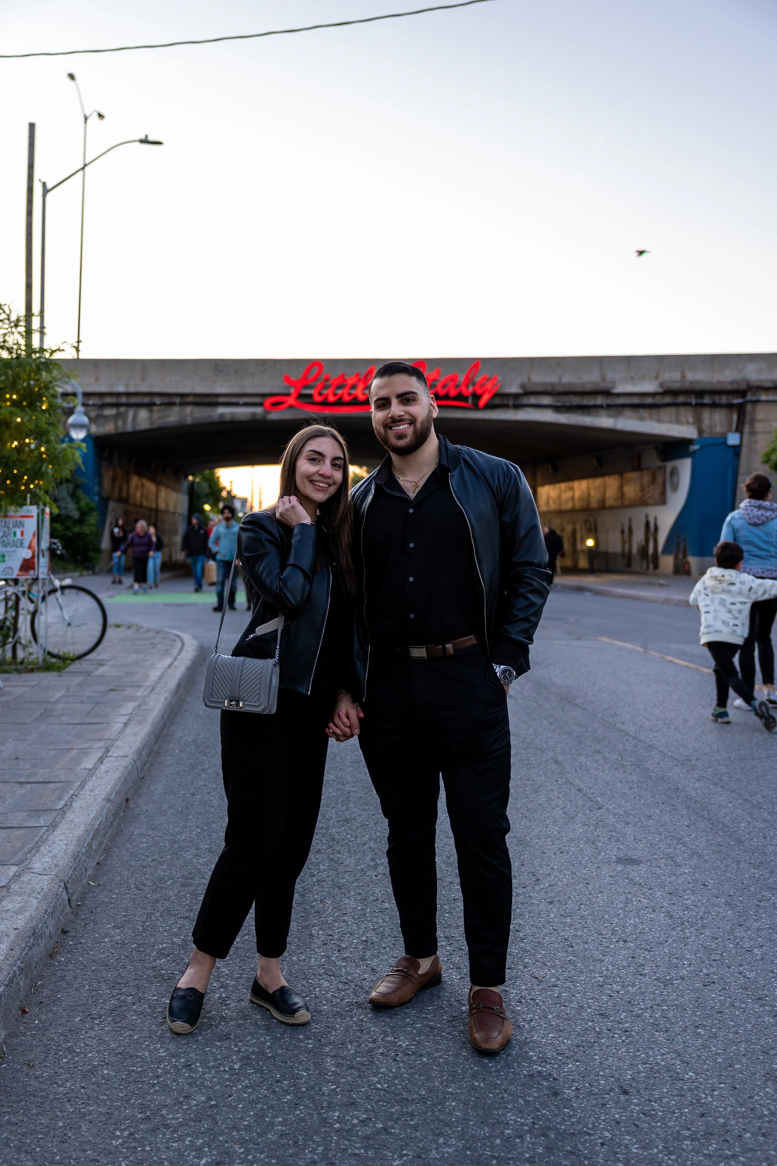 Couple holding hands on a street in Little Italy, with a neon sign overhead.