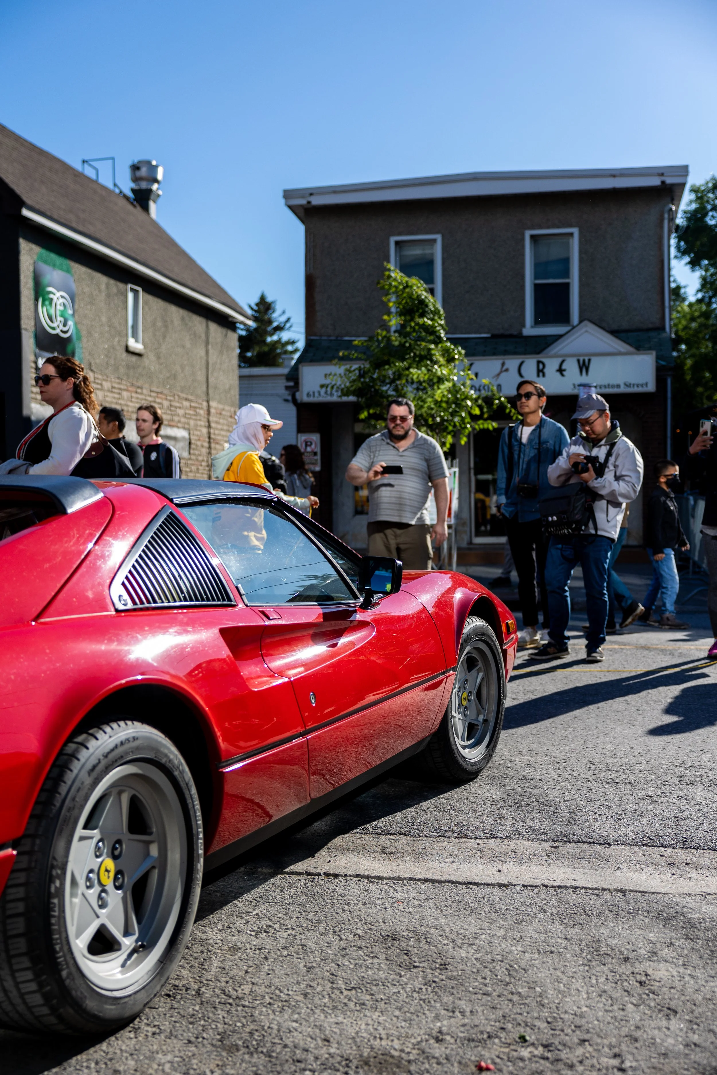 Red sports car in a parking lot with several people taking photos.