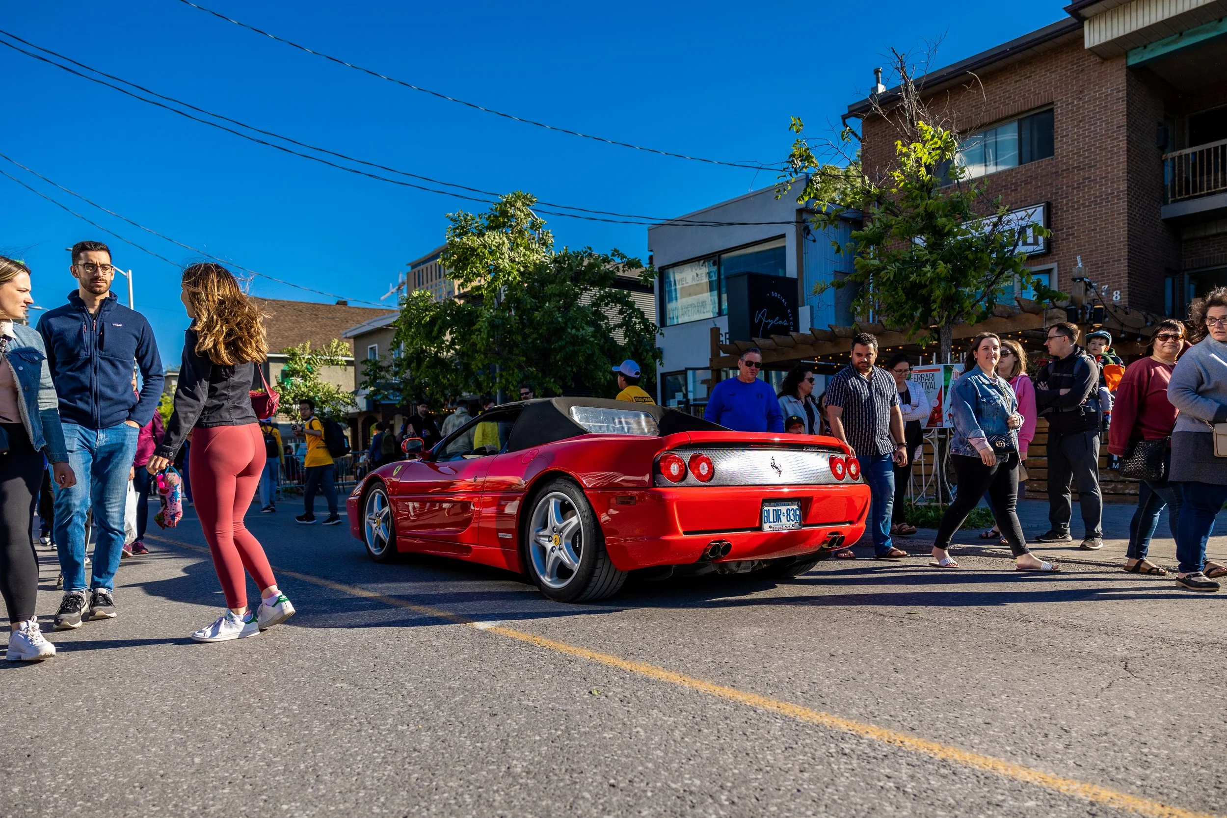 A red sports car parked on a street with people walking around in a busy urban setting on a sunny day.
