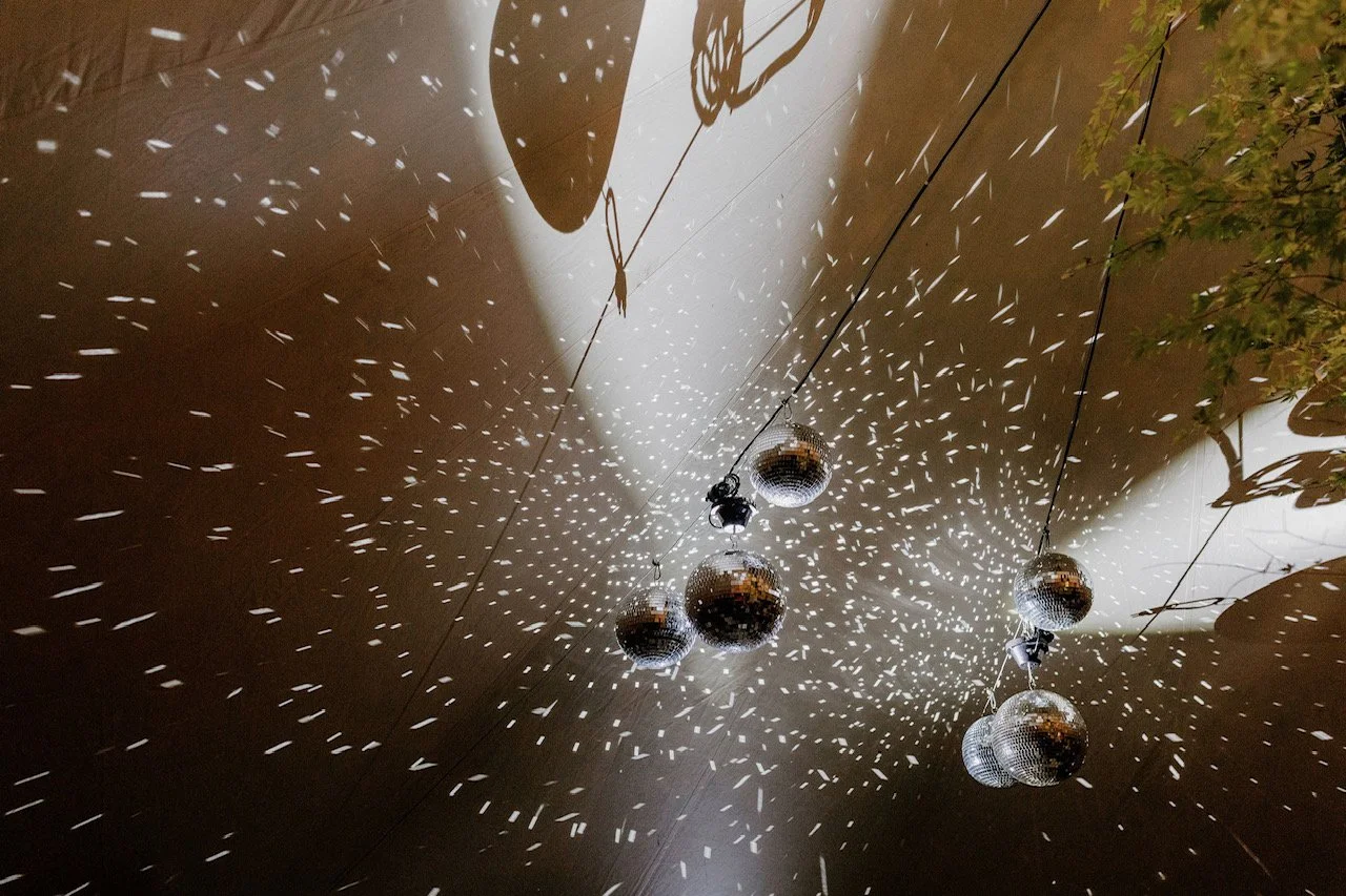 Multiple disco balls hanging from a ceiling, reflecting light and creating a star-like pattern on the ceiling and walls. Some shadows of the disco balls are also visible.
