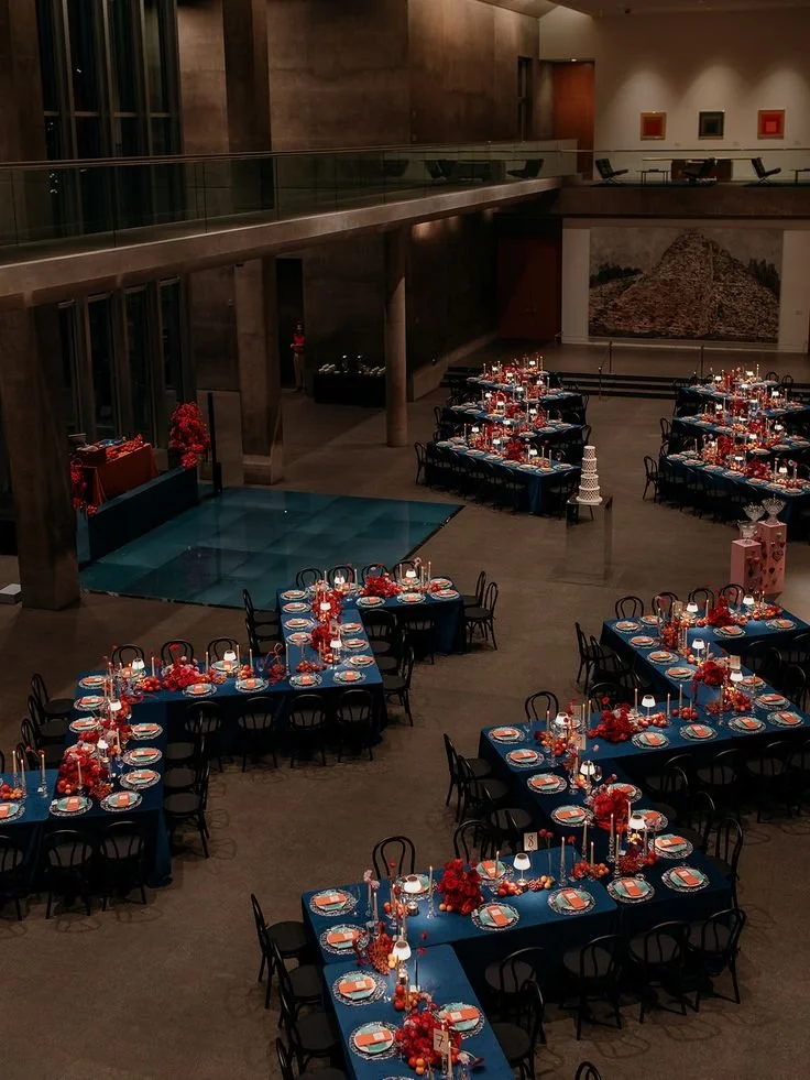 Serpentine tables with deep blue linen and red florals at a sky blue and maroon wedding reception