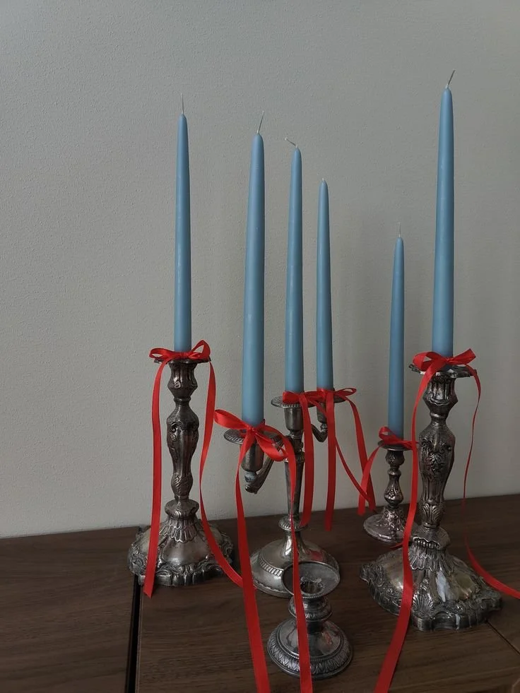 Blue taper candles tied with red ribbon in silver candlesticks for a sky blue and maroon wedding table