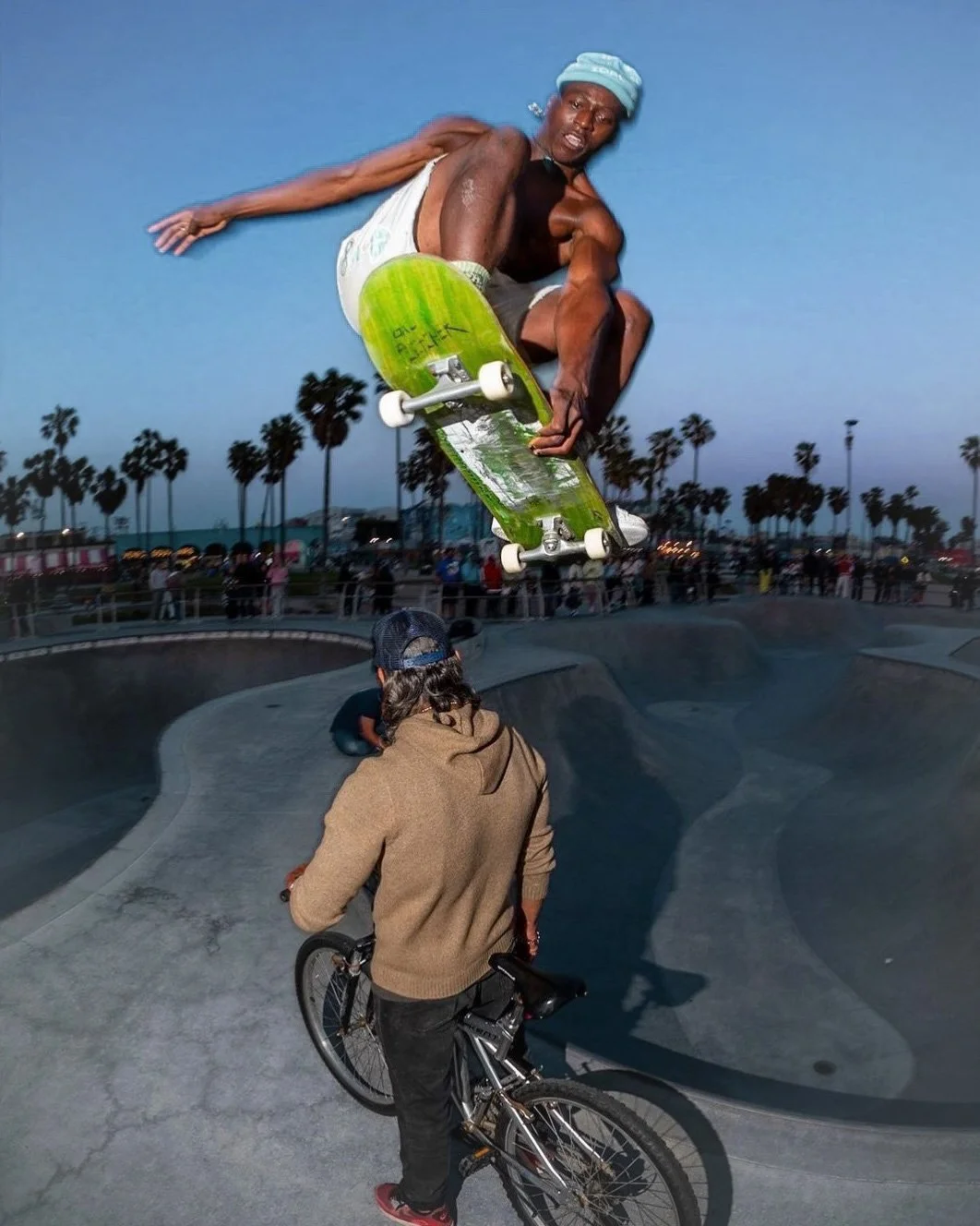 A skateboarder in mid-air performing a trick at a skate park during dusk, with palm trees in the background and onlookers watching.