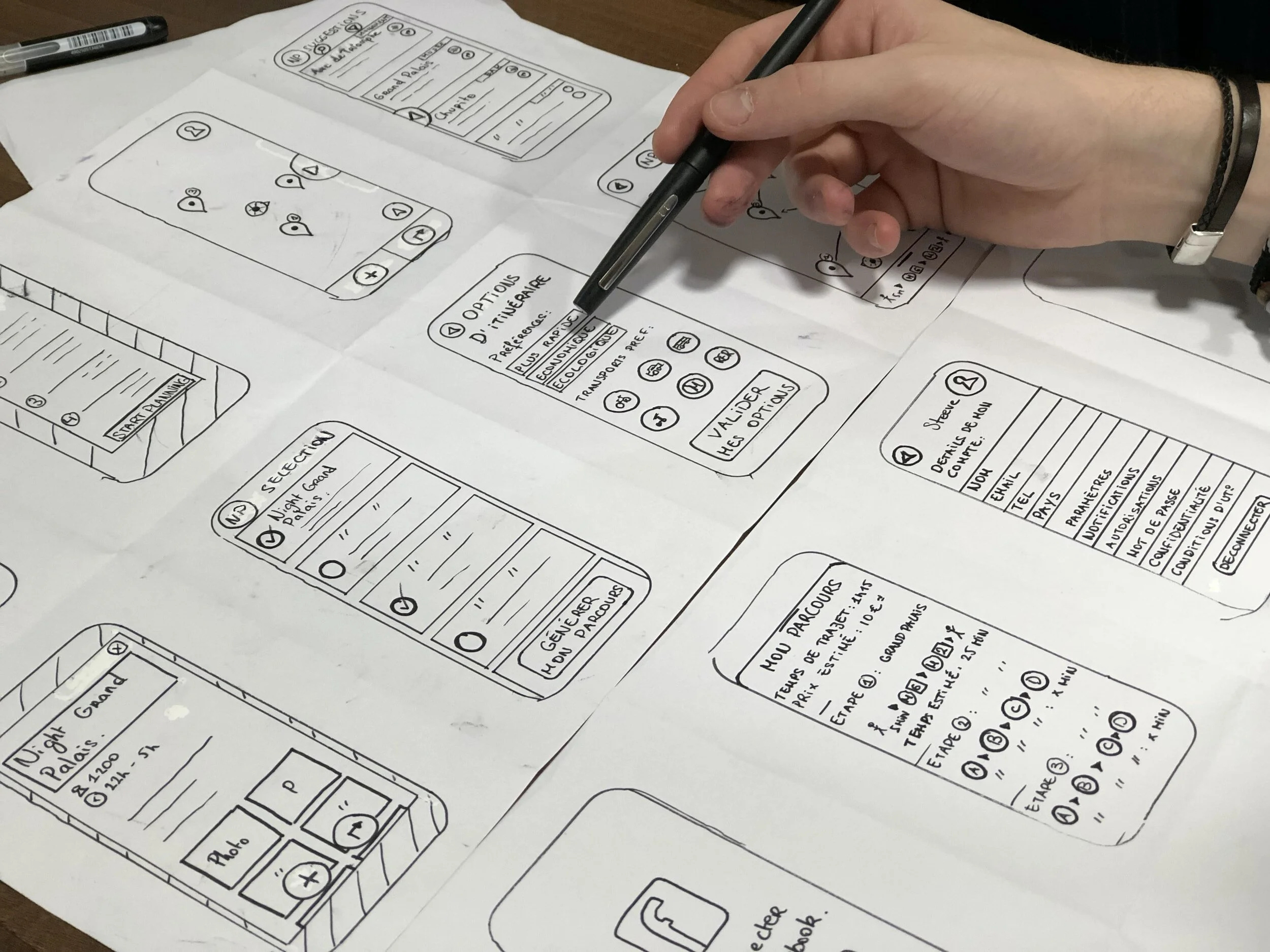Hand sketching and annotating wireframes and layout designs on paper, depicting mobile app screens and user interface elements.