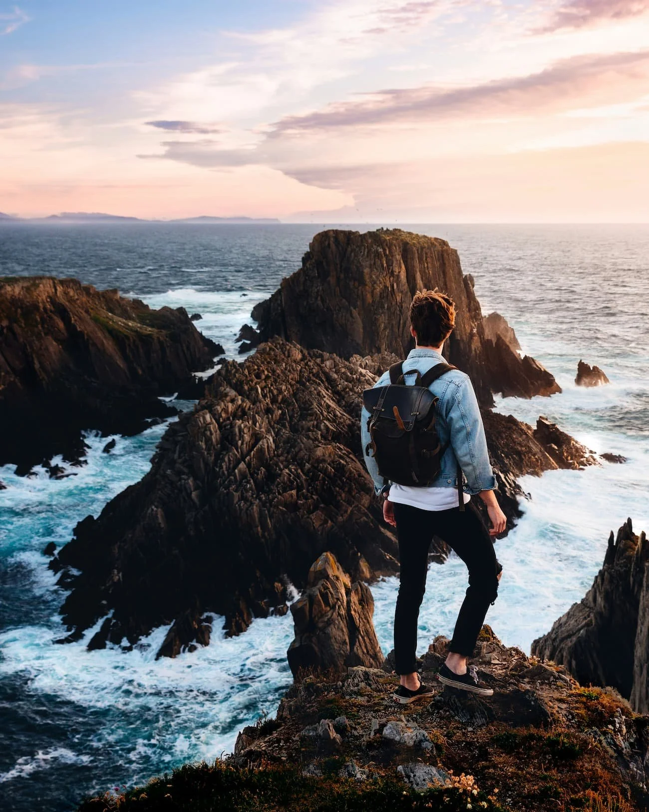 Traveller standing on coastal cliffs overlooking the ocean during a campervan road trip – illustrating different travel styles when choosing a VW campervan | which VW campervan size is right for you | Cornwall