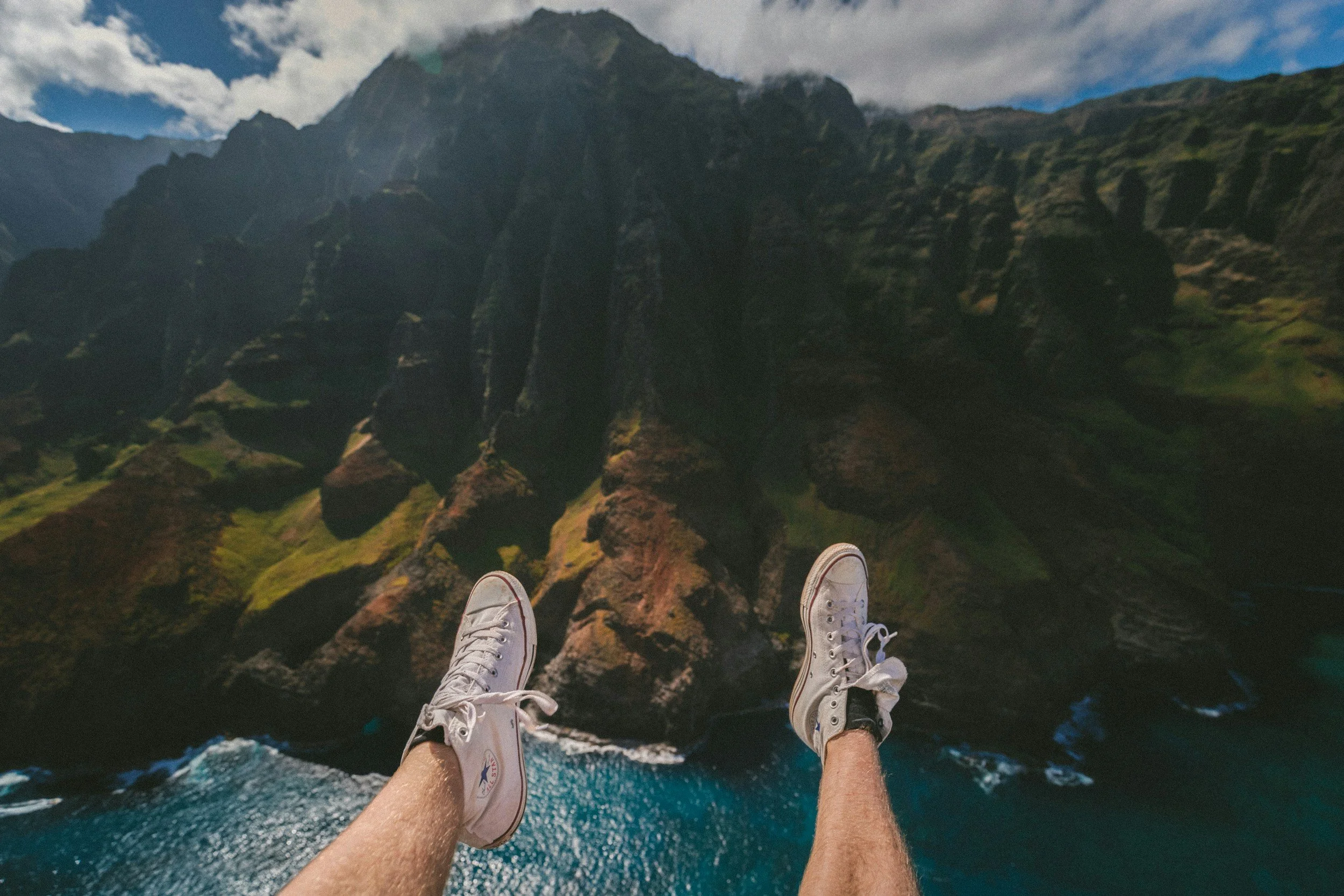 Person wearing white sneakers hanging above a scenic coastal cliffs and ocean view.