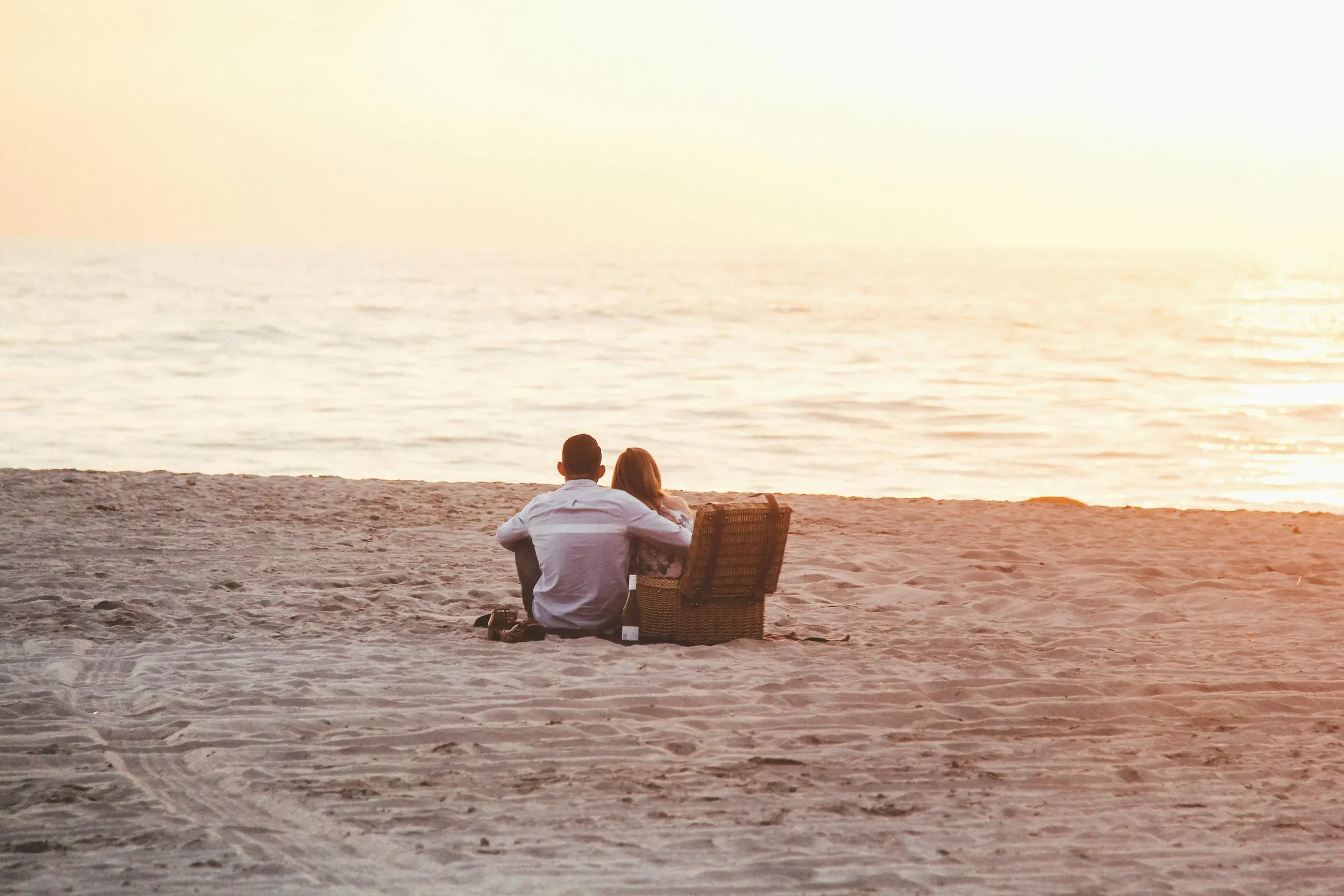 A couple sitting on the sandy beach watching a sunset over the ocean | The Estuary premium camper van conversion | Cornwall