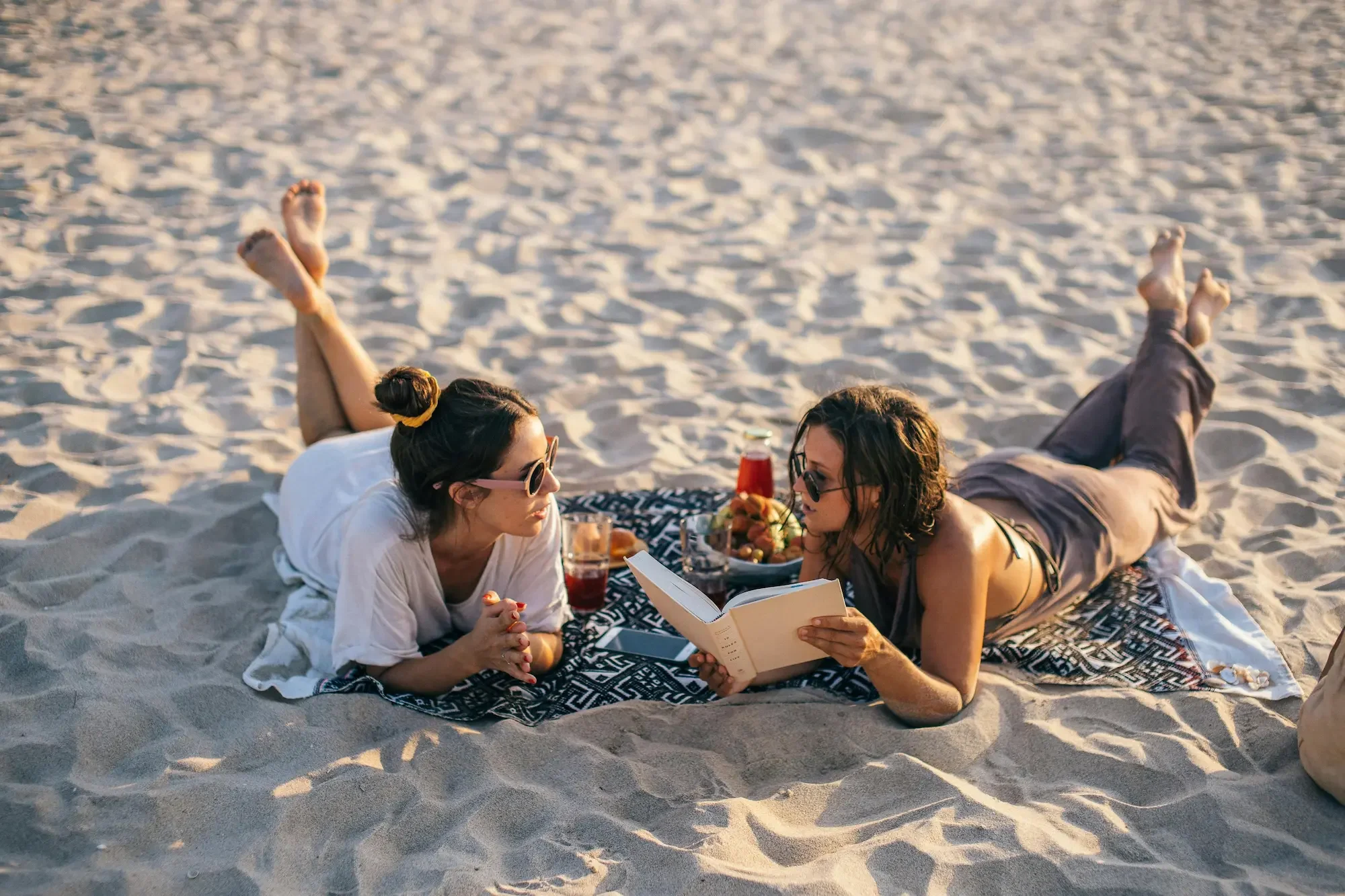Two women lying on a beach blanket on the sand | The Dune weekend campervan conversion | Cornwall