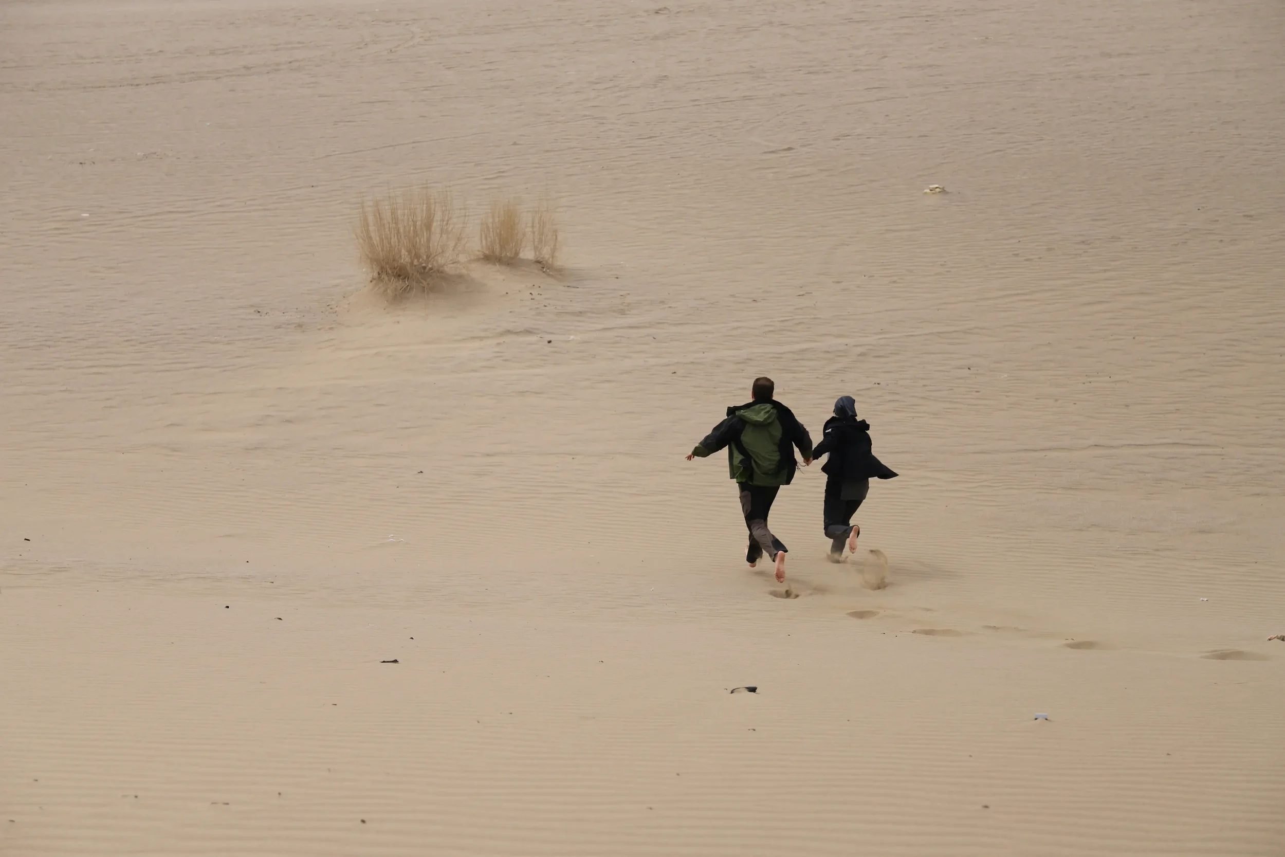 Two carefree people running across the sand dunes, leaving footprints behind | The Dune weekend campervan conversion | Cornwall