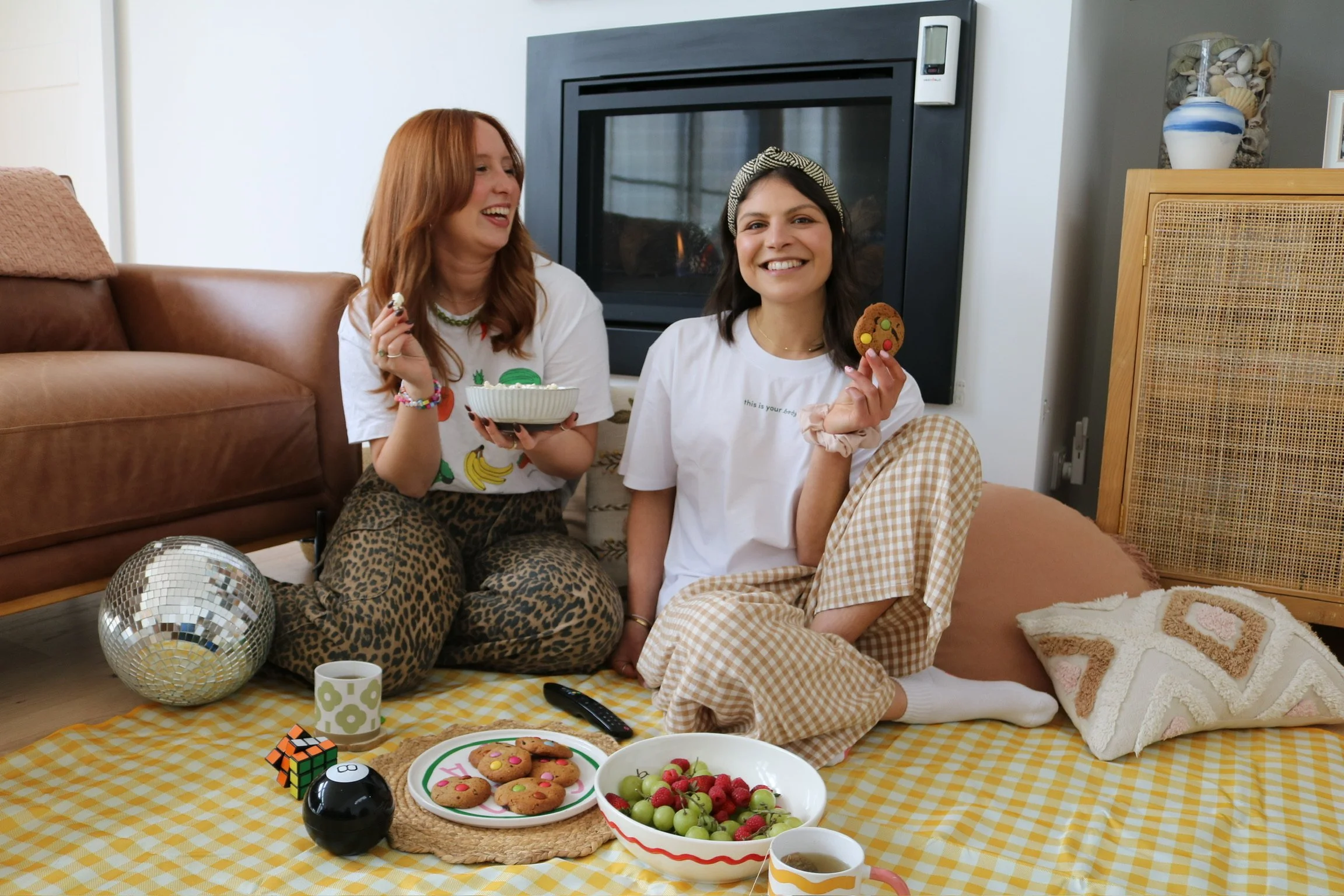 Gel, founder of This is Your Body, laughing on a picnic rug with cookies, popcorn and fruit