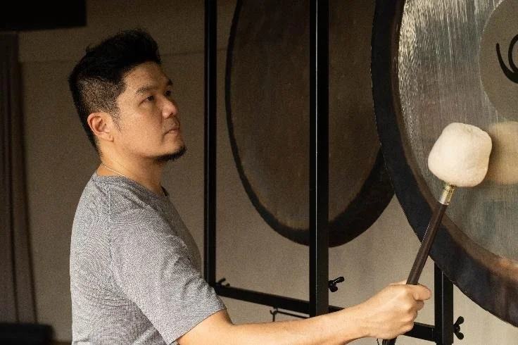 A young man playing a large gong with a mallet in an indoor setting.