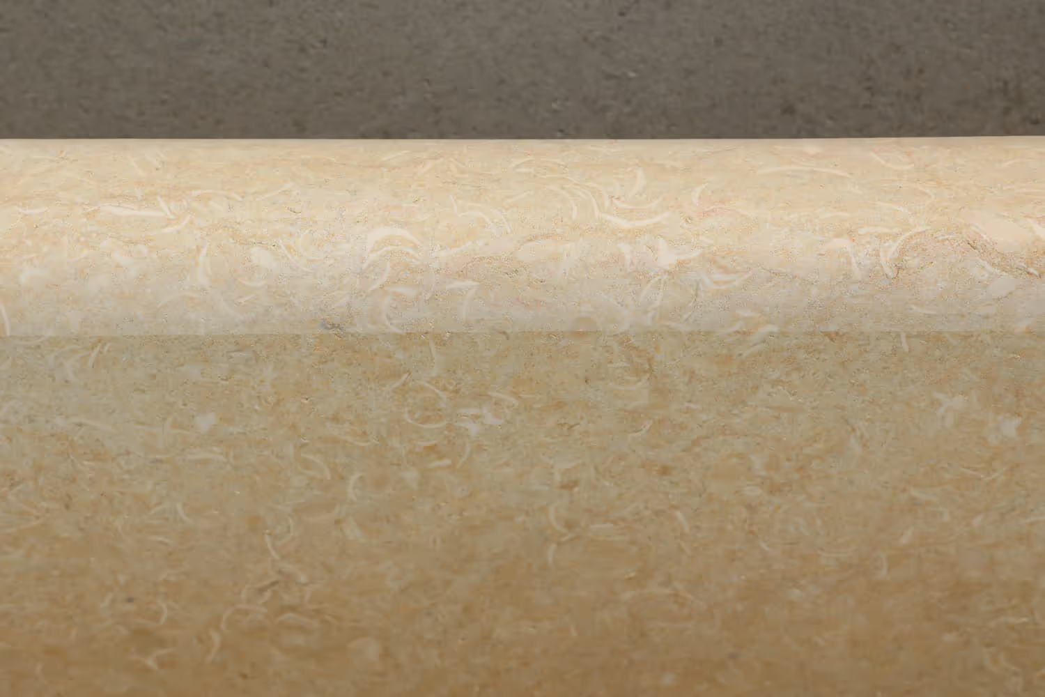 A smooth, beige countertop with a textured, light pattern, set against a dark brown wall.