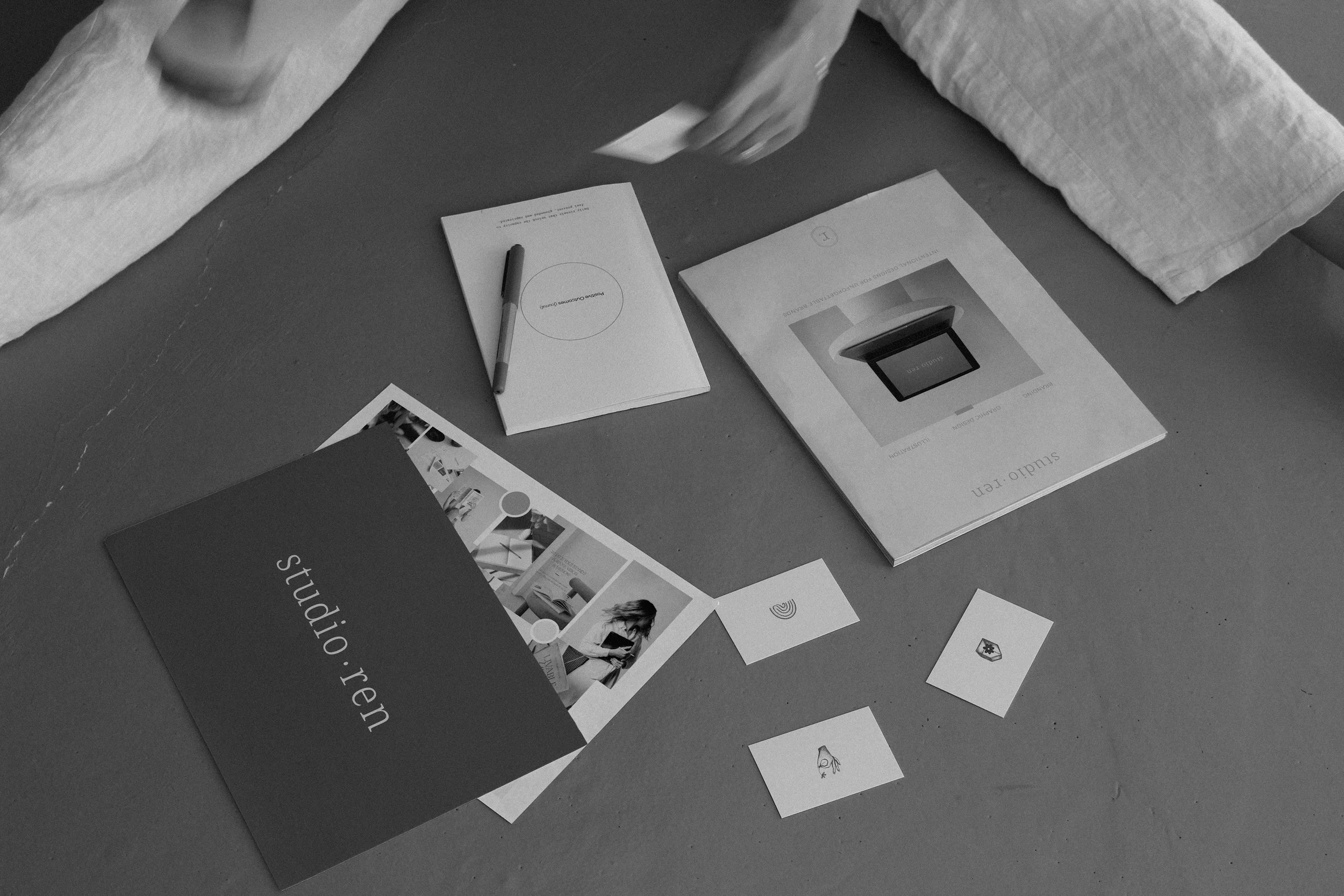 A view of the floor with various printed materials, including a Studio Ren flyer, a moodboard, and notes, along with a pen and business cards.