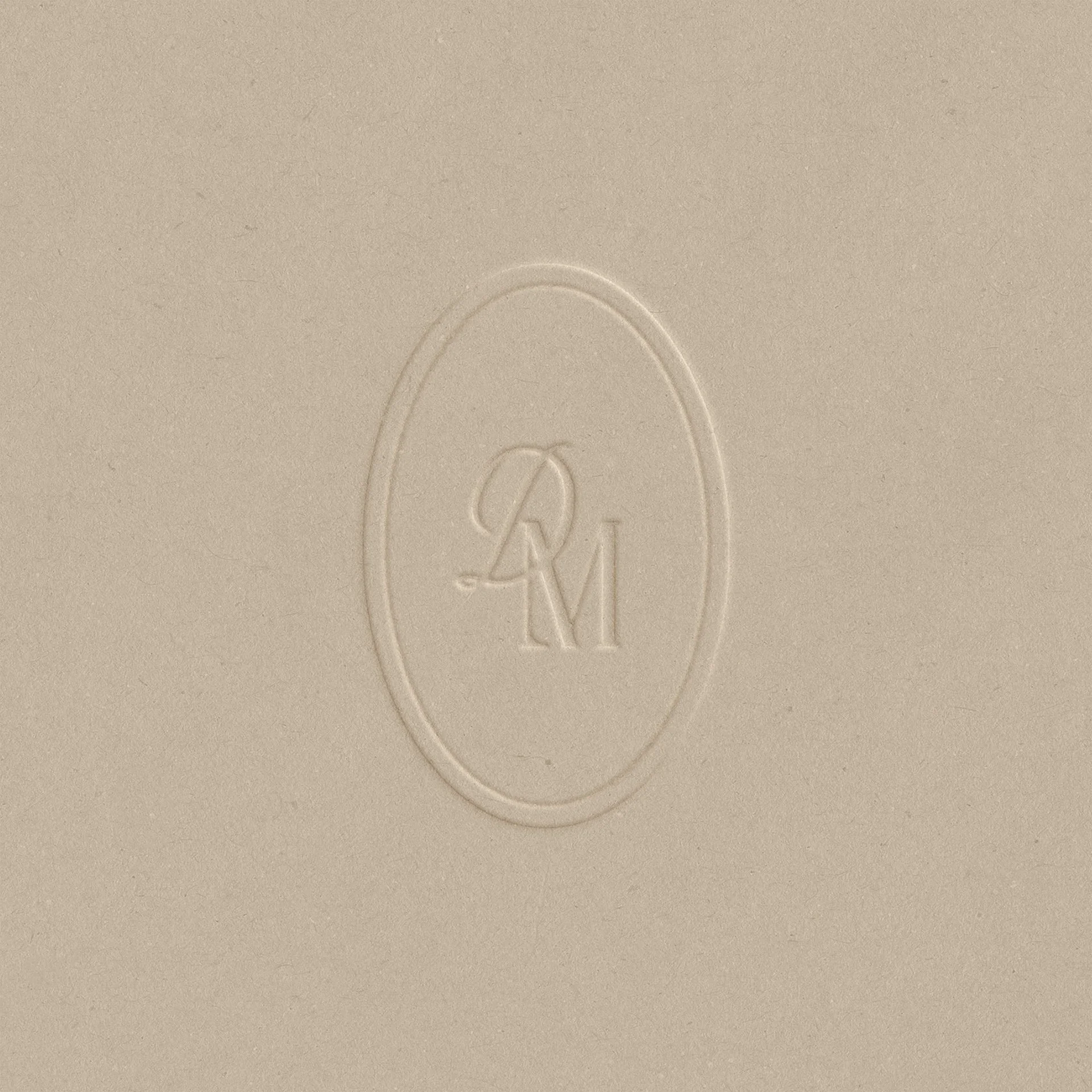 Close-up of a textured beige surface with an embossed oval logo containing the initials 'Q' and 'M'.