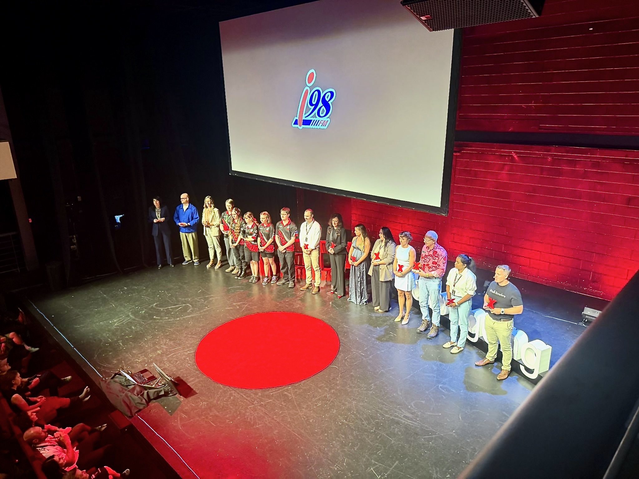 Dr Meghan Dares standing with fellow speakers on stage at TEDxWollongong 2026.