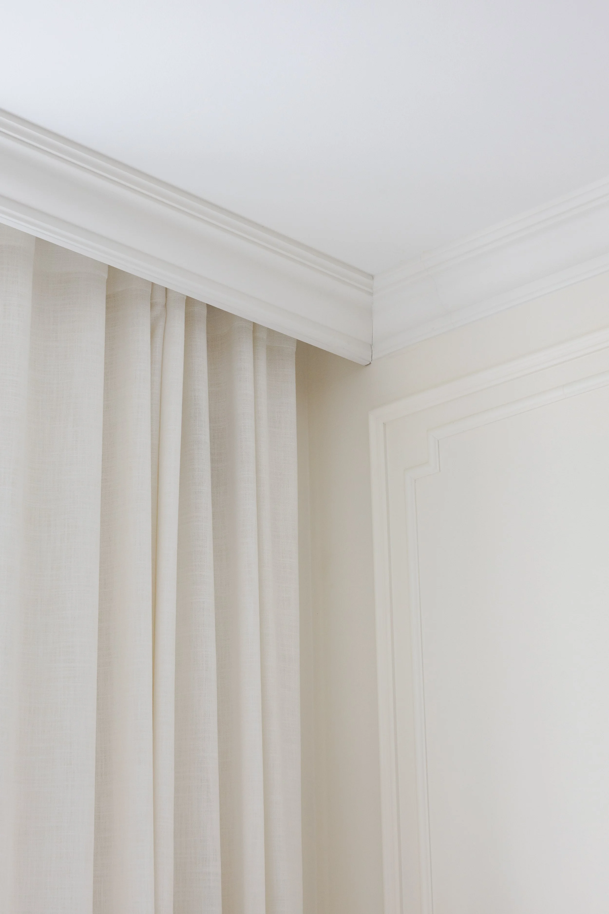 Crown moldings hide the curtain rails. Walls are painted in a warm white