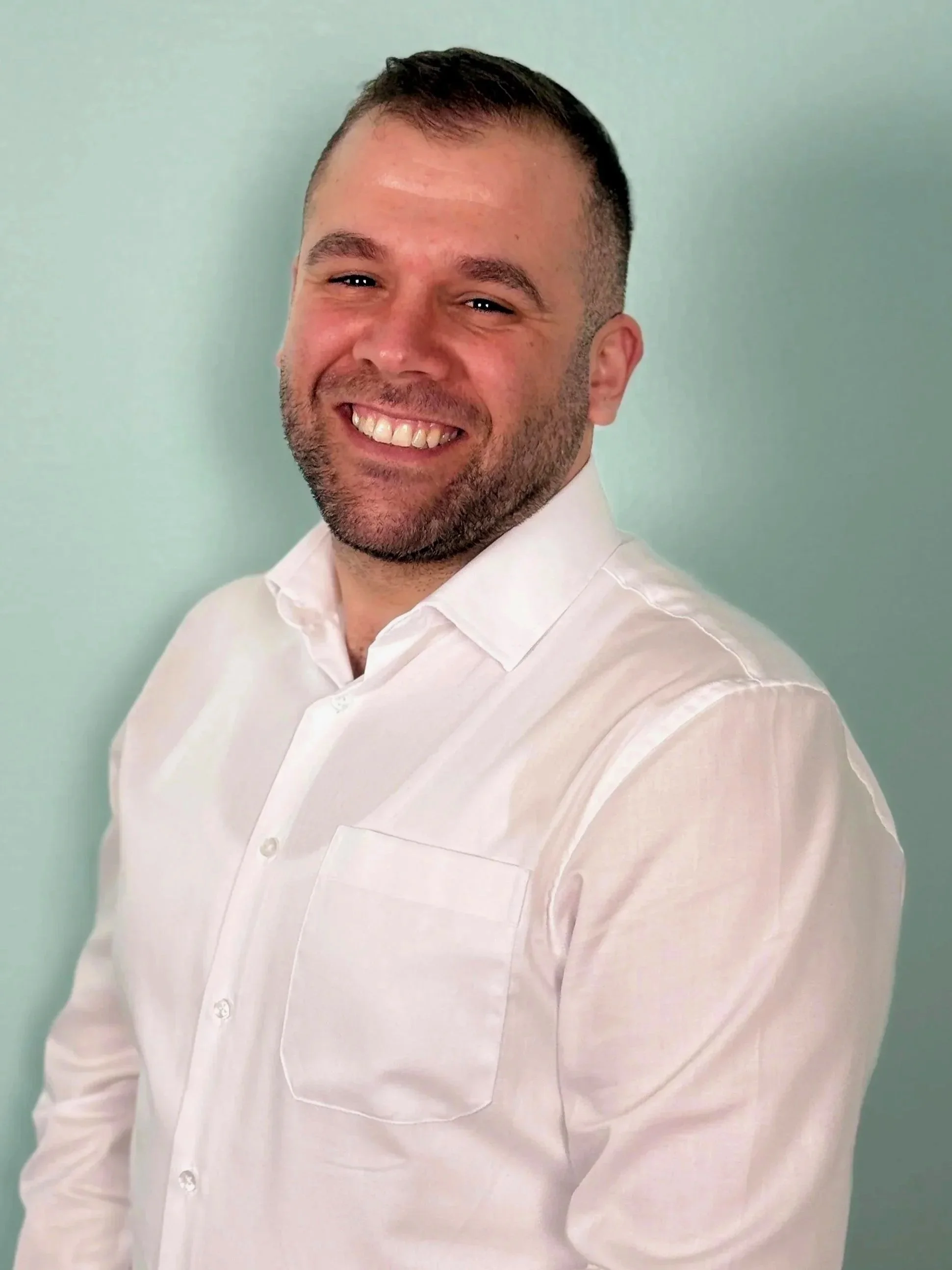 Lächelnder Mann in Weiß vor hellgrünem Hintergrund.