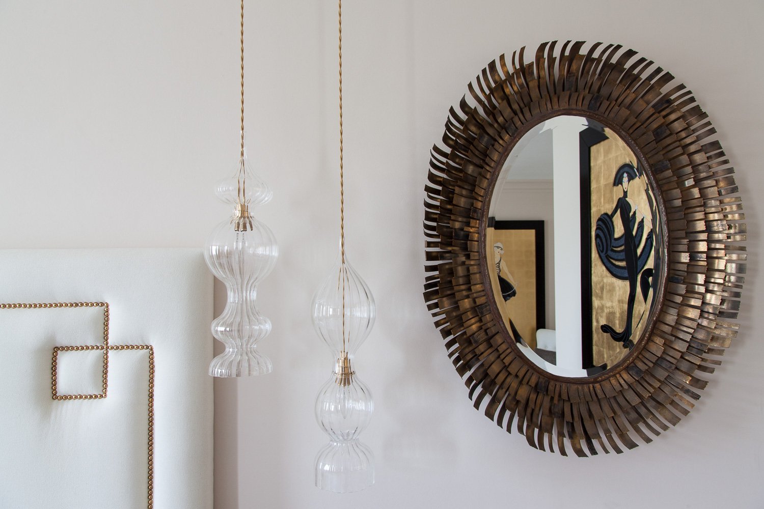 Close-up of sunburst mirror and sculptural glass pendant lights above a studded headboard, interior design photographer, Clapham