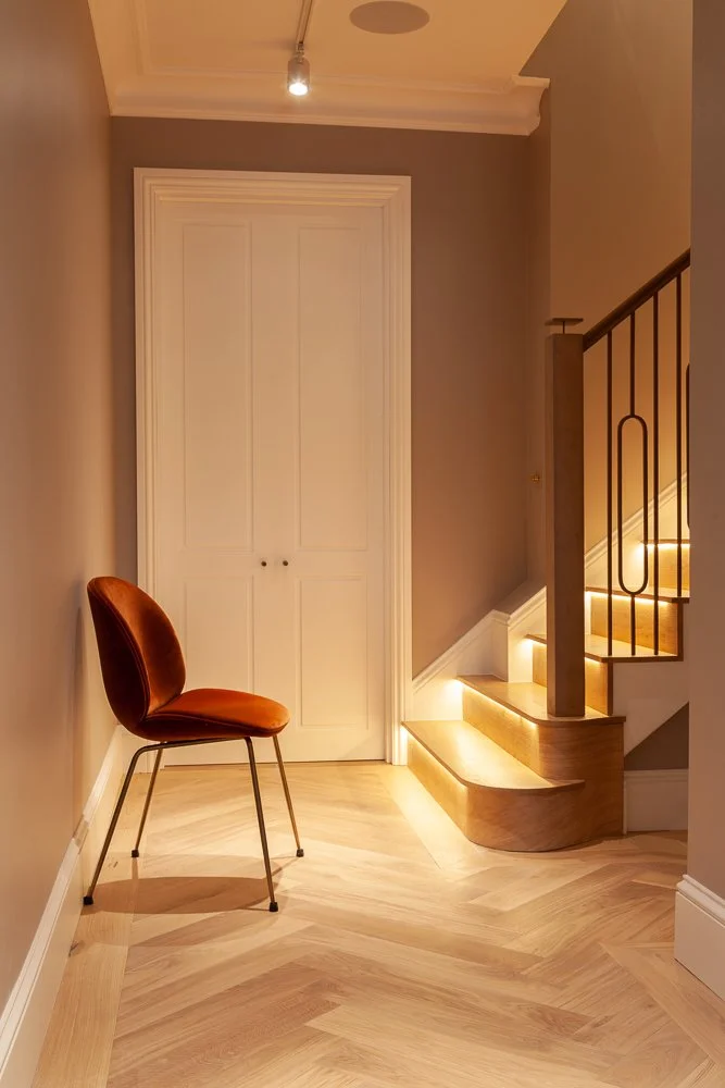 Hallway with herringbone flooring, orange accent chair and illuminated staircase, interior photographer London, Mayfair