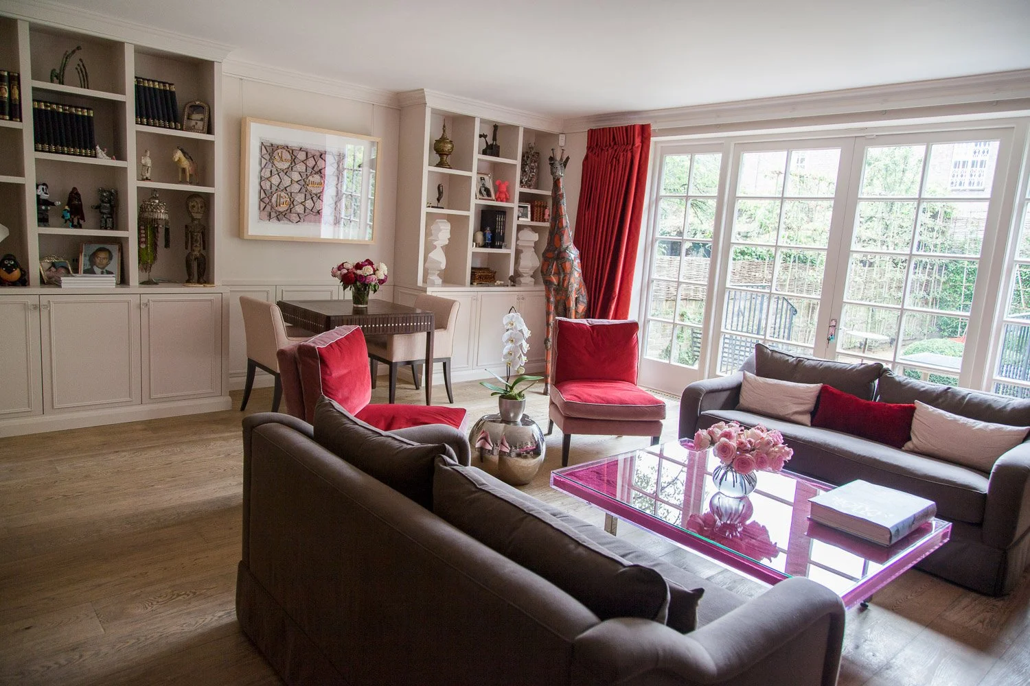 Open-plan living space with built-in shelving, red curtains and pink accent table, interior photographer London, Chelsea