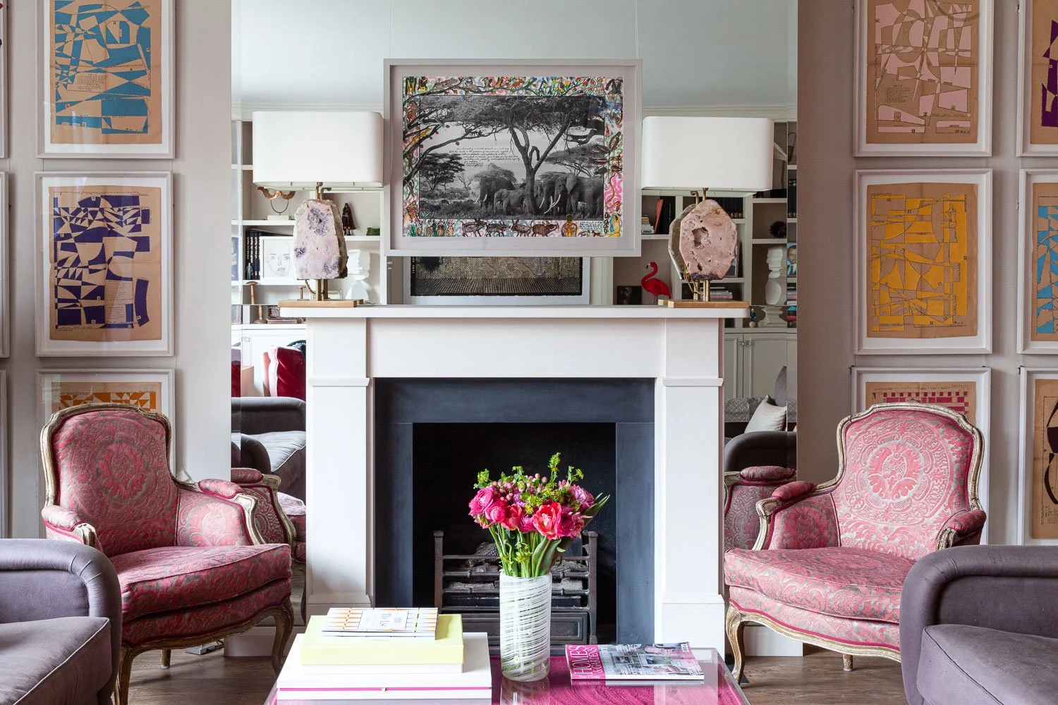 Sitting room with pink accent chairs beside a fireplace and framed art collection, interior design photographer London, Chelsea