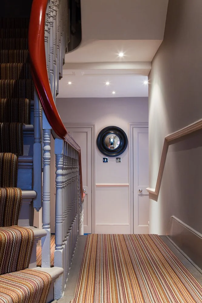 Striped stair runner on a curved staircase with wrought-iron balustrade, interior photography, Chelsea