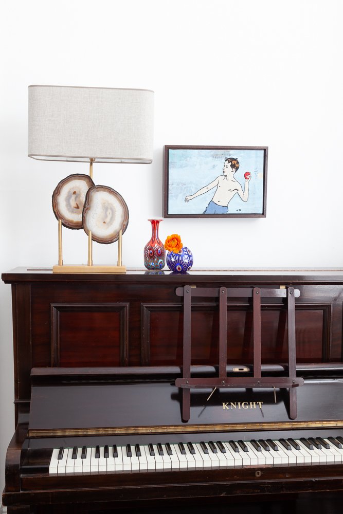 Isabelle Bizard mineral stone table lamp with a Murano glass vase, styled on a piano, interior photography