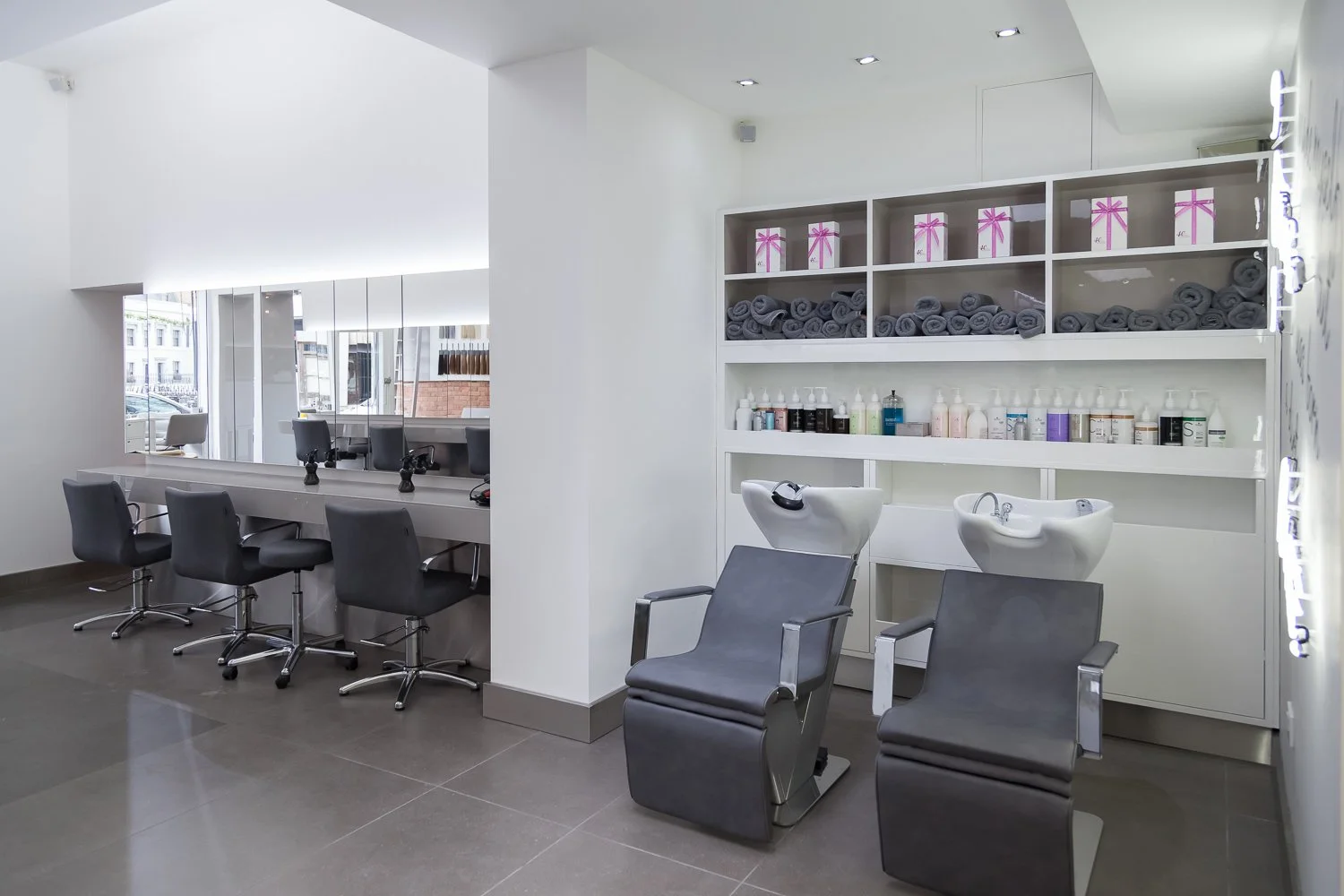 Hair salon wash area with grey styling chairs and product shelving, interior design photographer