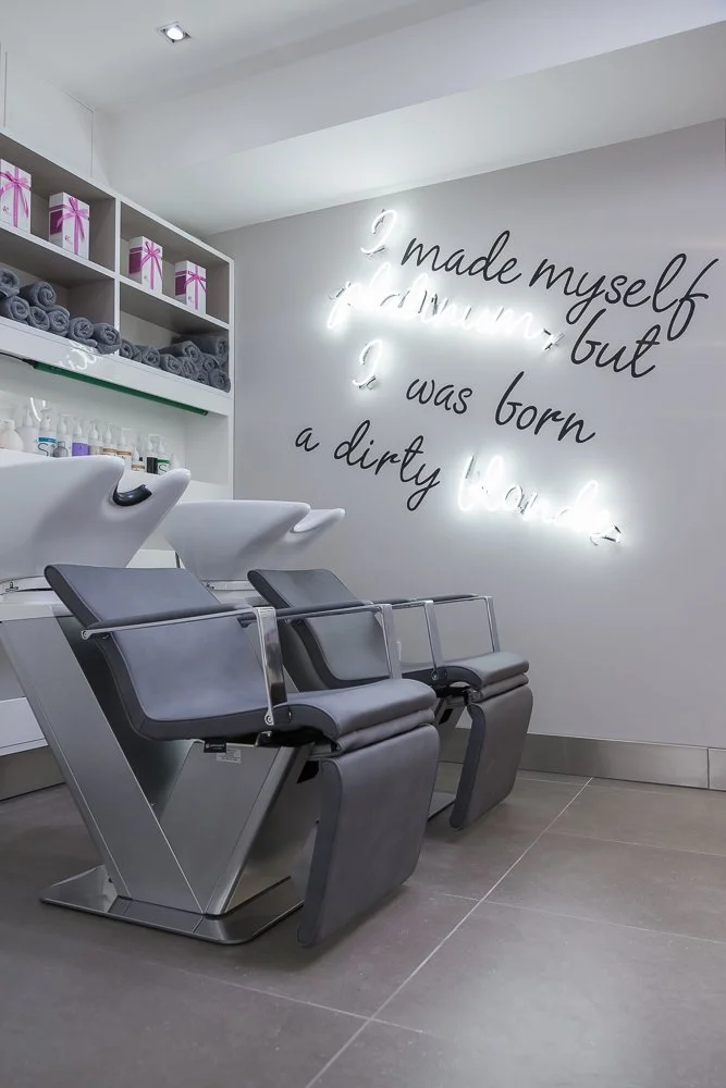 Close-up of hair salon wash chairs with illuminated neon quote wall, interior photography