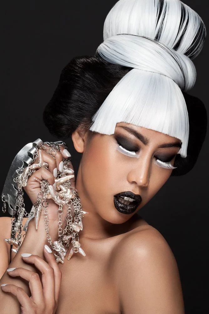 Model with a sculpted white fringe and black lips, silver statement necklace wrapped around her hand, styled and art directed by Laurence Trolet, brand photographer