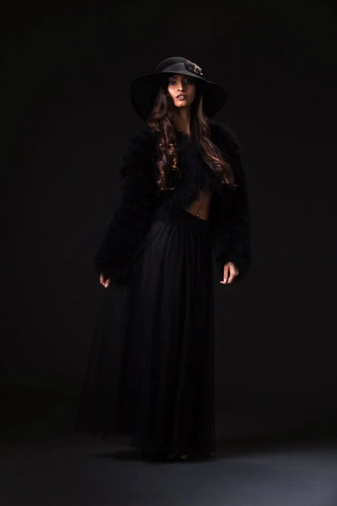 Full-length portrait of a model in a black wide-brim hat, black jacket and long black skirt, styled and art directed by Laurence Trolet, branding photography