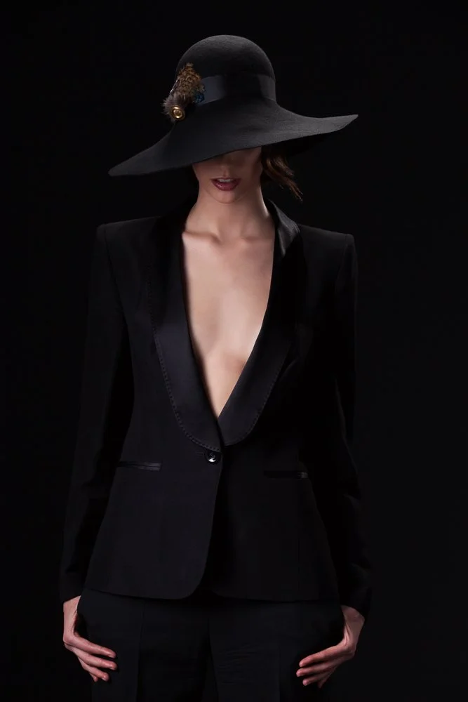 Model in a black wide-brim hat with a gold feather detail and a black tuxedo jacket, styled and art directed by Laurence Trolet, brand photographer