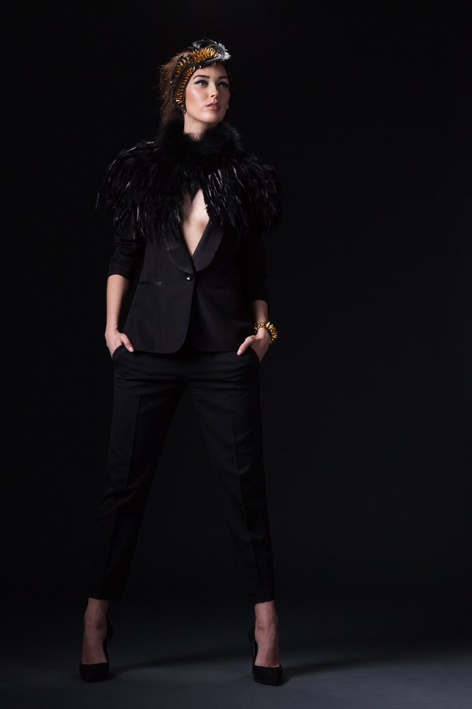 Full-length portrait of a model in a feathered headpiece, black feather cape and trouser suit, styled and art directed by Laurence Trolet, brand photography