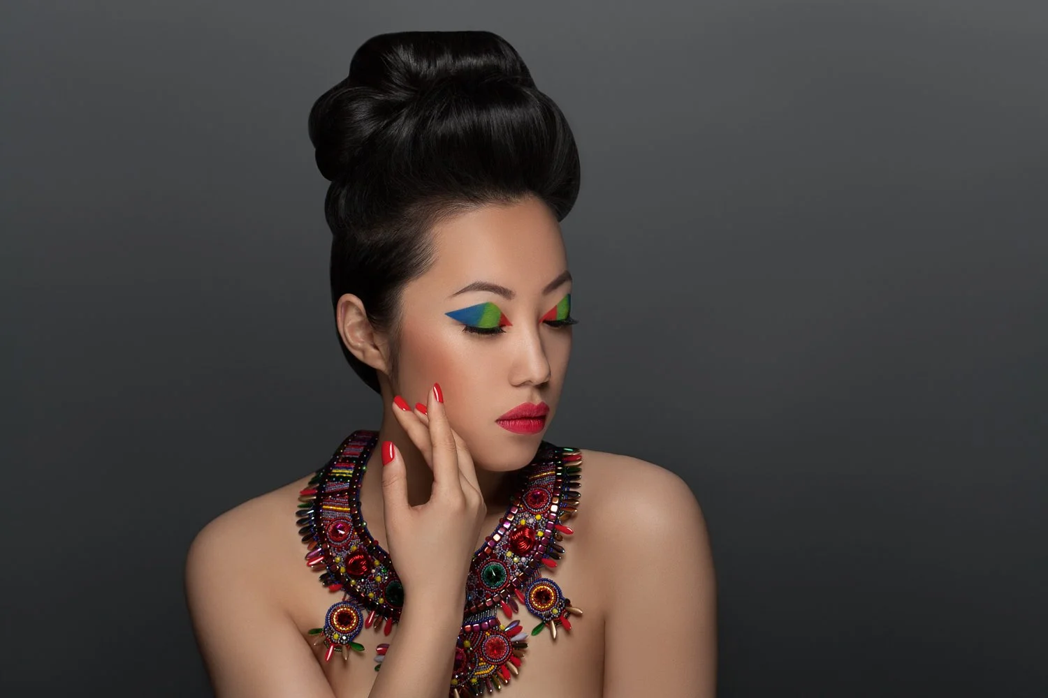 Model with a hand raised to her chin against a grey backdrop, wearing an ornate beaded necklace, styled and art directed by Laurence Trolet, branding photography