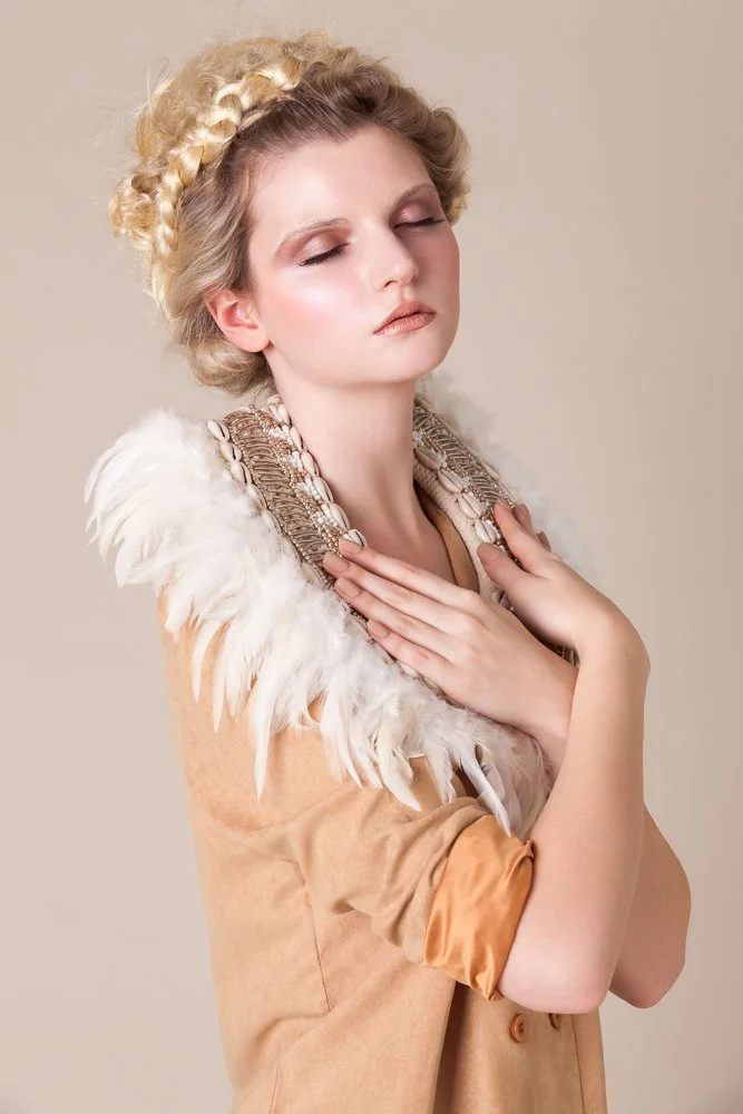 Close-up portrait of a model with a feathered shoulder collar and braided headpiece, styled and art directed by Laurence Trolet, editorial fashion photography